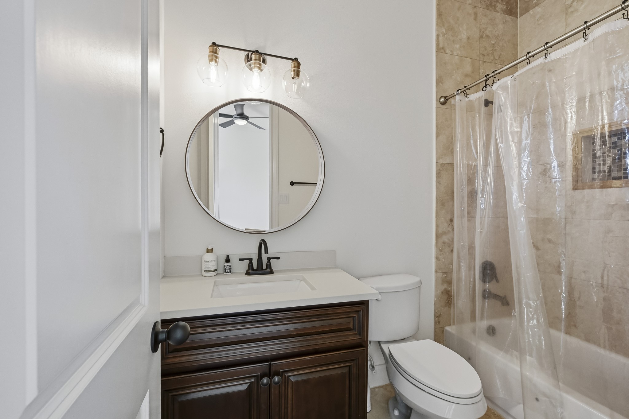 Elegant bathroom featuring a modern round mirror, stylish vanity with dark wood cabinetry, and a shower with natural stone tile.