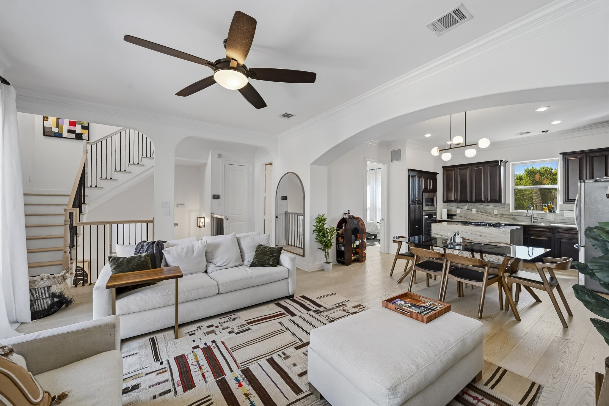 Bright and open living space featuring comfortable seating, stylish area rug, and a seamless flow into the dining area and kitchen with dark cabinetry and stainless steel appliances.