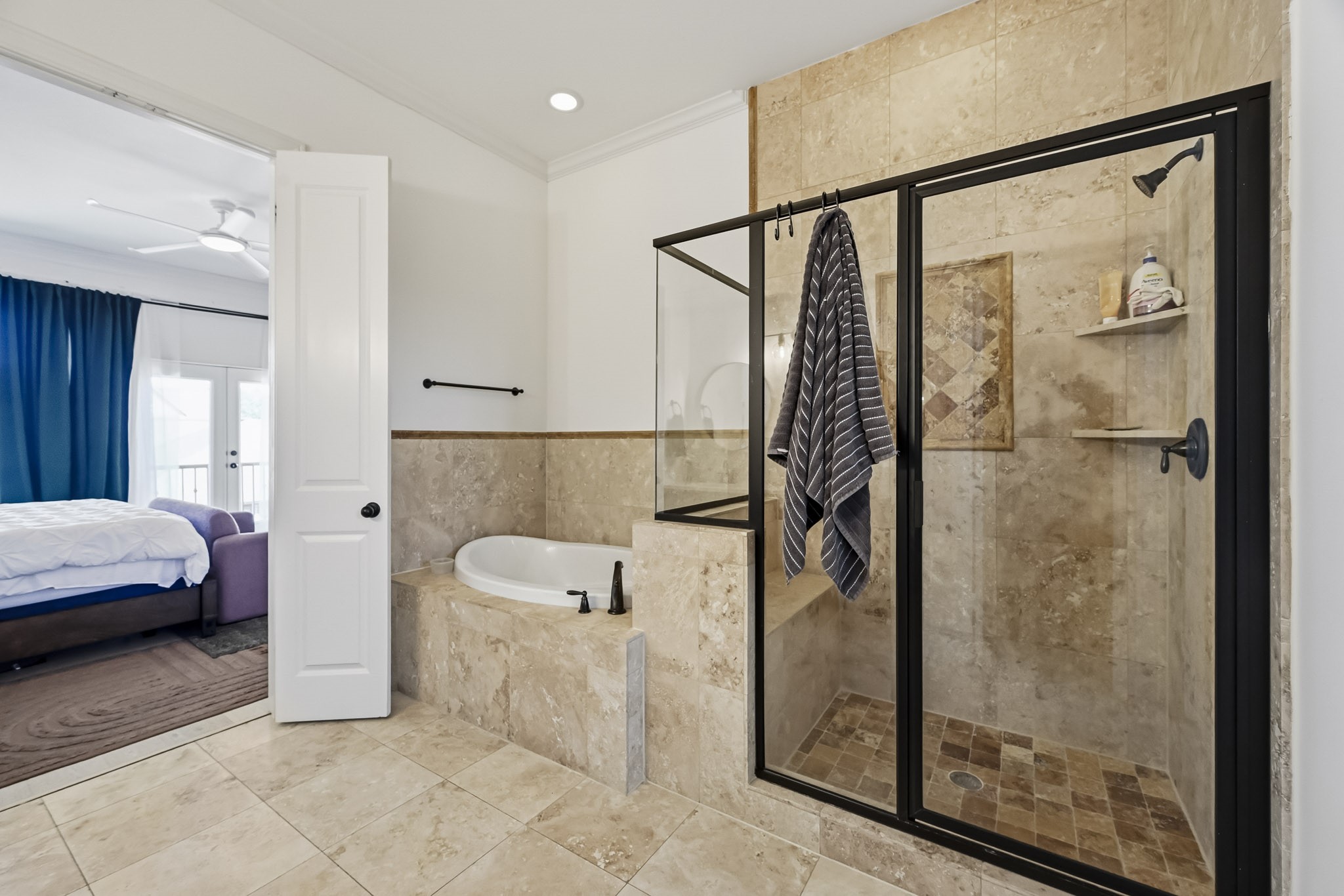 Elegant bathroom featuring a spacious glass-enclosed shower and luxurious soaking tub, with direct access to a cozy bedroom.