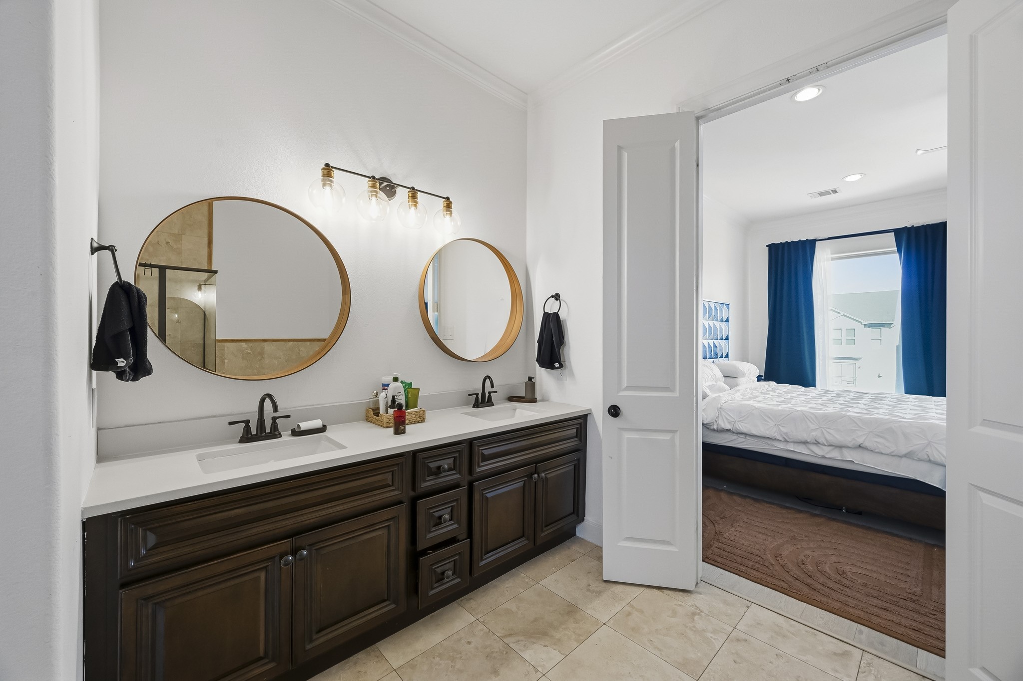 Elegant bathroom with dual vanity, stylish round mirrors, and modern fixtures, seamlessly leading into a bright bedroom with a cozy atmosphere.