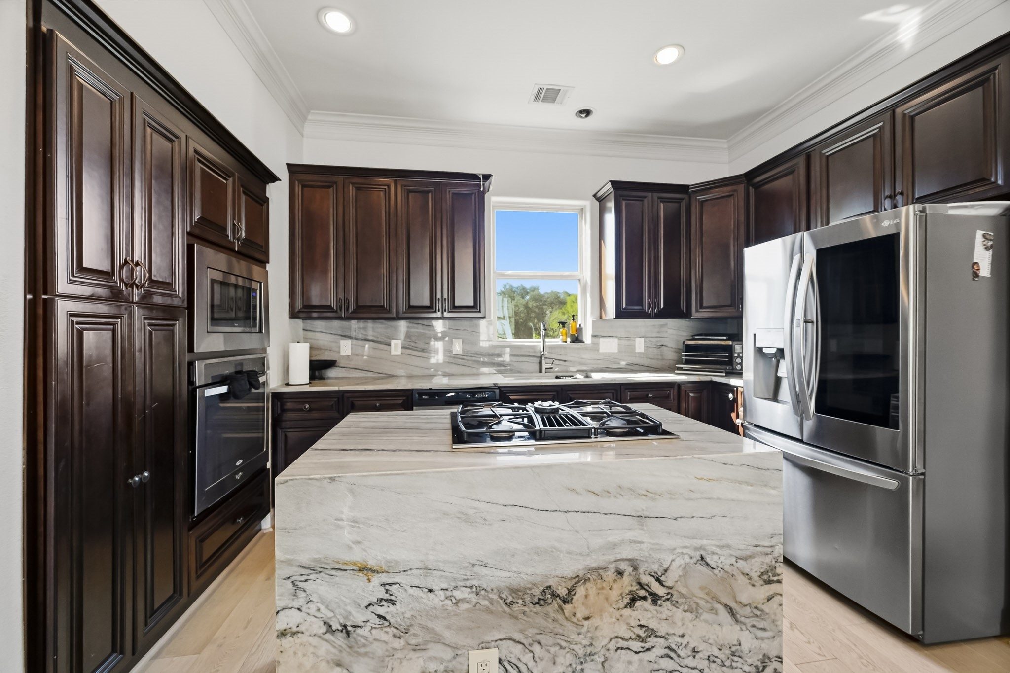 Elegant kitchen featuring rich dark wood cabinetry, a sleek marble island with a built-in cooktop, and modern stainless steel appliances.