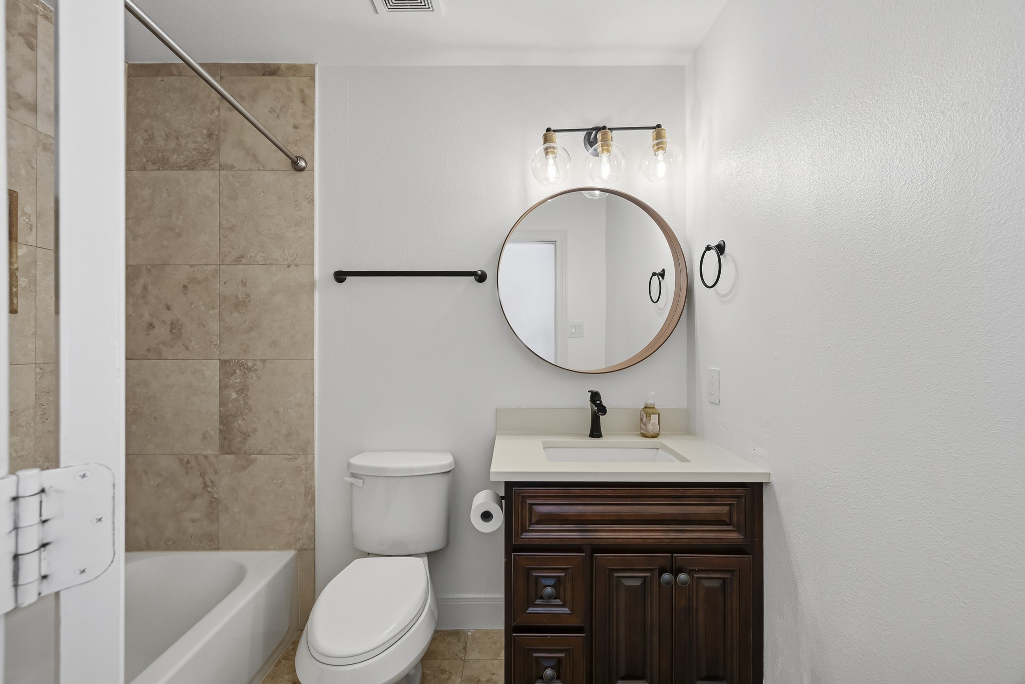 Charming bathroom featuring a modern vanity with a round mirror and elegant lighting, complemented by a tiled shower and neutral tones.