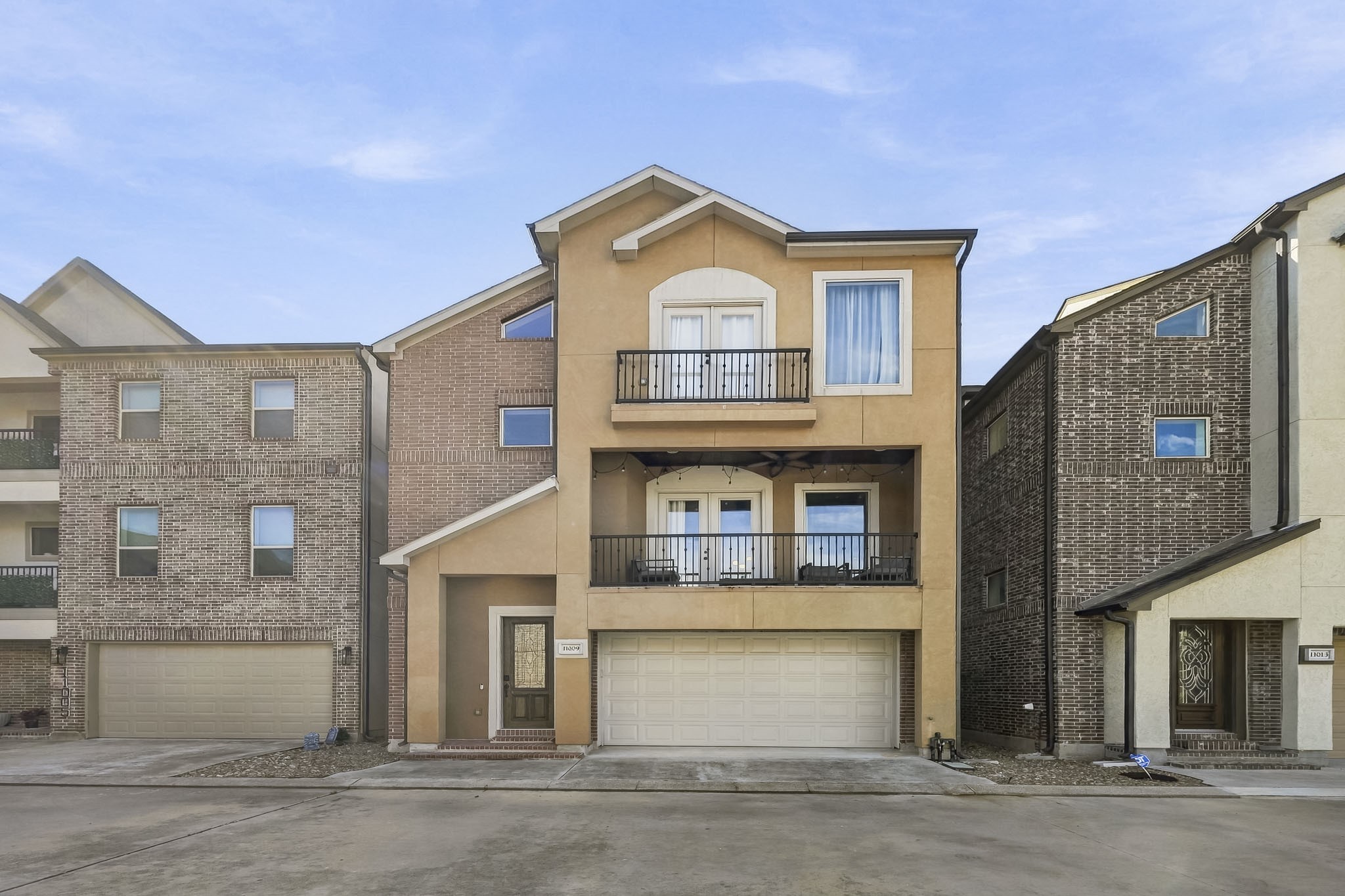 Modern three-story townhouse with a warm, inviting facade, featuring two balconies and a spacious two-car garage.