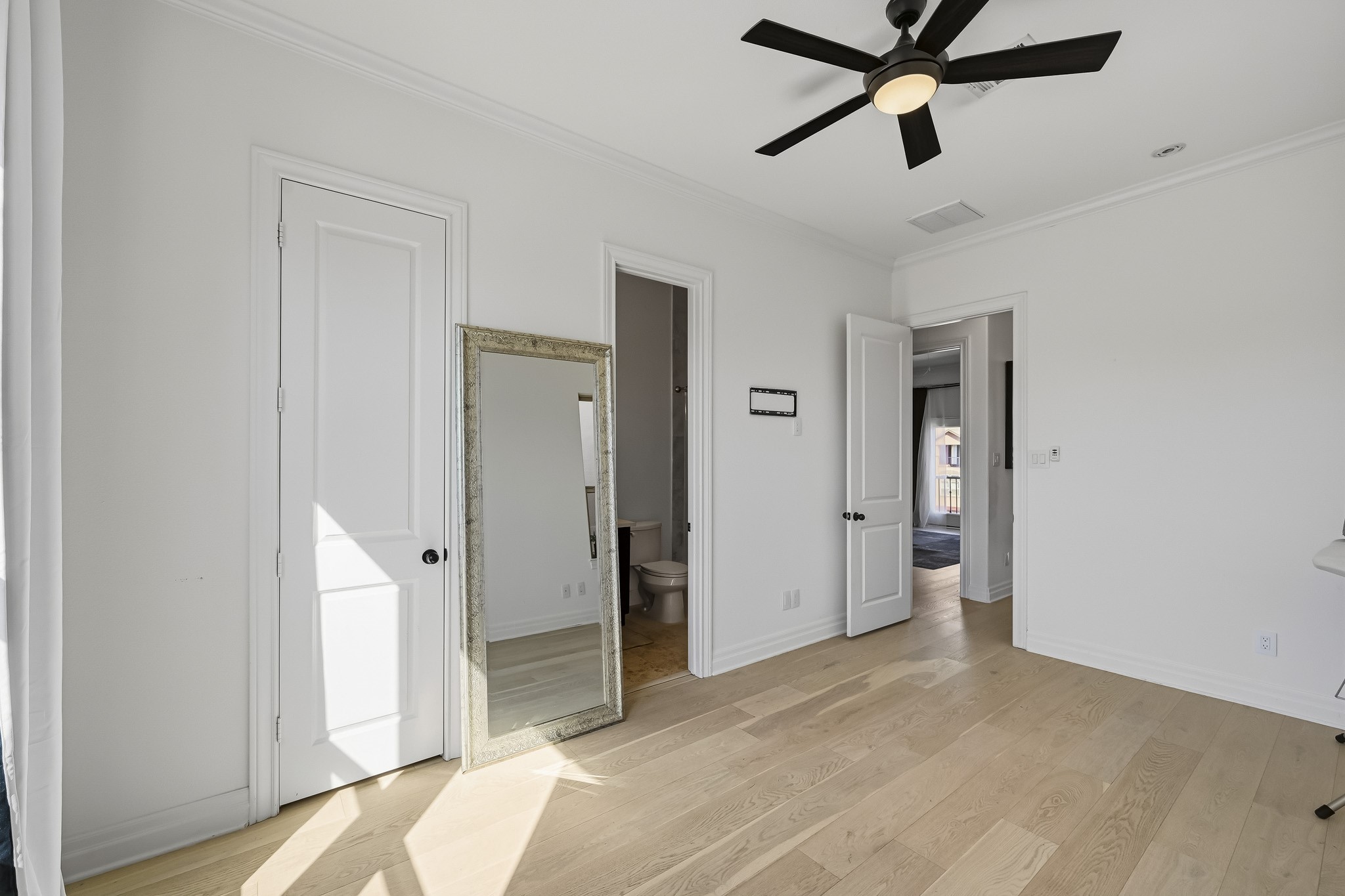 Bright and airy room featuring light hardwood floors and ample natural light, with convenient access to an attached bathroom.