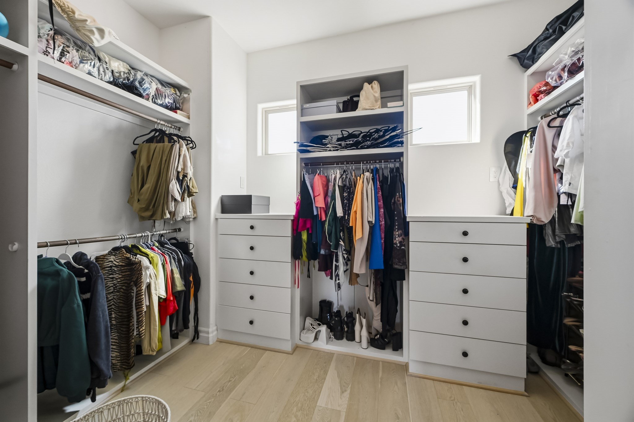 Spacious walk-in closet with ample storage, featuring built-in shelves, drawers, and hanging space, accented by natural light from two small windows.