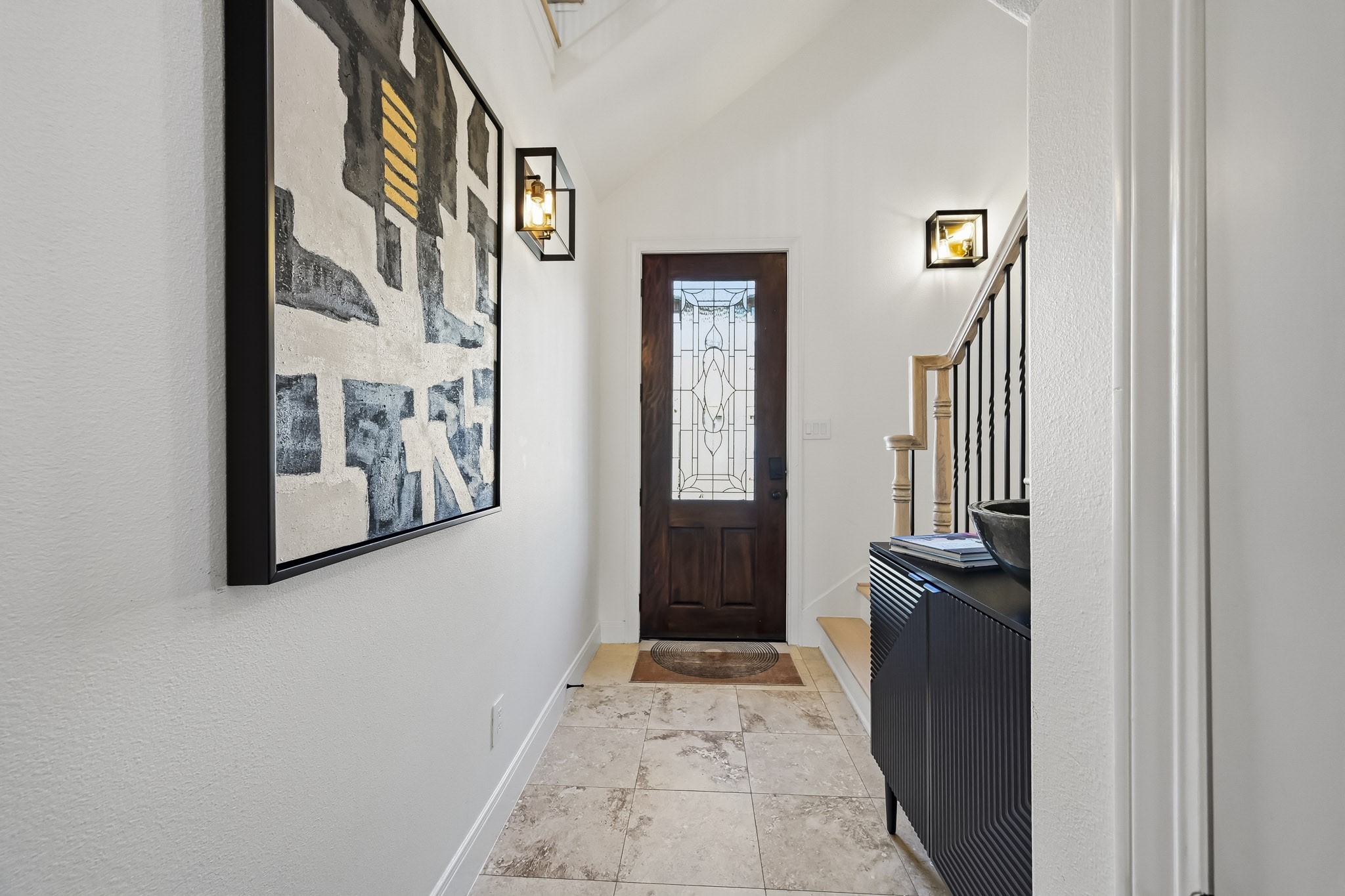 Inviting entryway featuring a stylish wooden door with decorative glass, elegant tile flooring, and modern wall sconces.