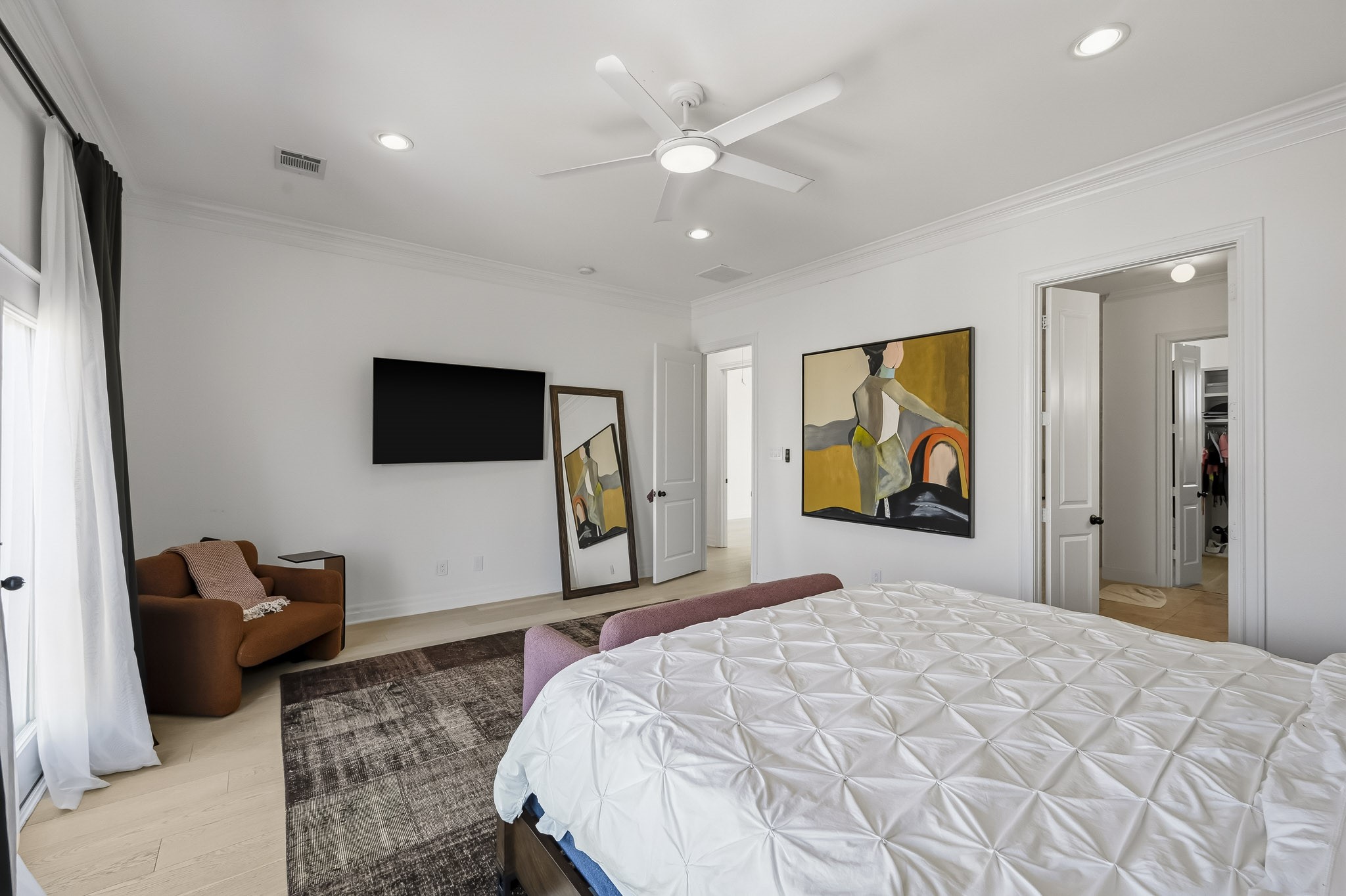 Spacious bedroom featuring modern decor, a cozy seating area, and a wall-mounted TV, with ample natural light and an attached bathroom.