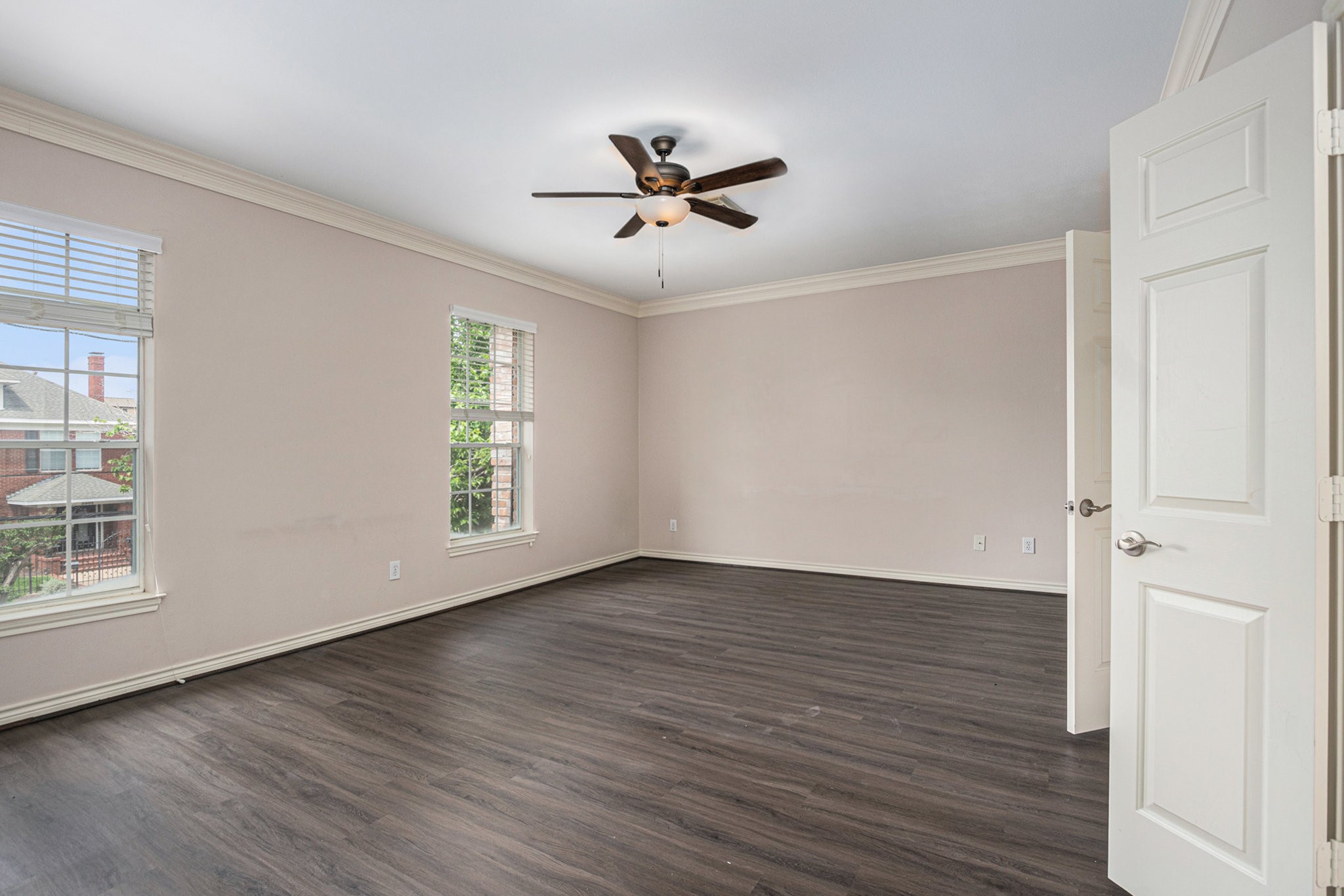 Spacious, bright room with large windows, neutral walls, and dark wood flooring. Features a ceiling fan and ample natural light, ideal for a bedroom or office.