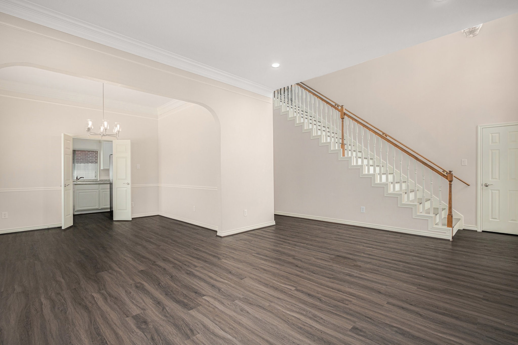 This spacious, light-filled living area features elegant dark wood flooring, a charming chandelier, and a classic staircase. It opens to a dining area with double doors leading to the kitchen, offering a seamless flow for entertaining.