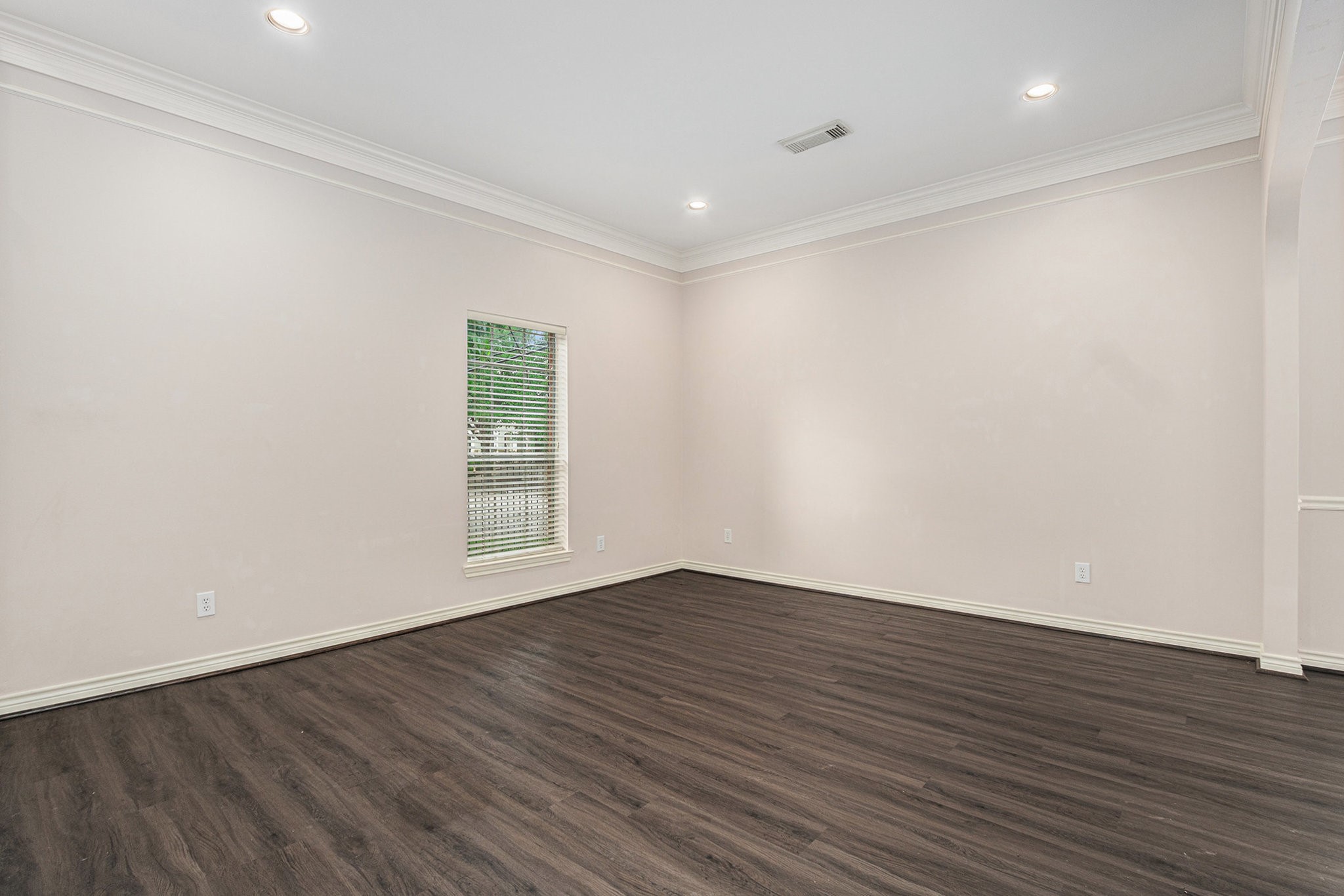 This spacious room features sleek dark wood flooring, neutral walls, and recessed lighting, creating a modern and inviting atmosphere. A large window brings in natural light, enhancing the room's bright and airy feel.