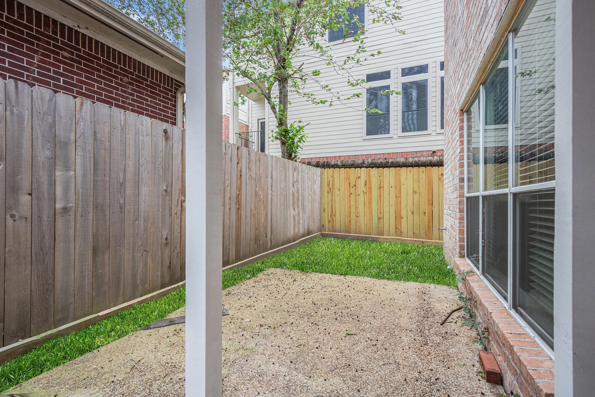 Cozy backyard space bordered by a wooden fence. Large windows provide natural light and a view of the yard. Perfect for a small garden or outdoor seating.