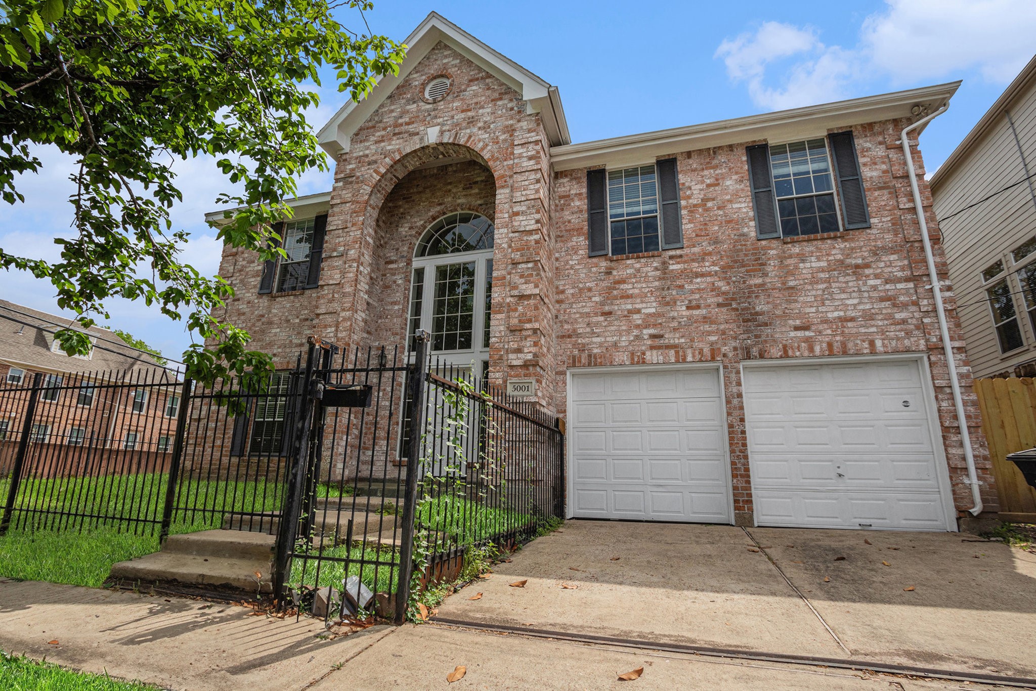 Two-story brick home with an elegant arched entrance and large windows. Features a double garage and a fenced front yard, offering both security and charm.