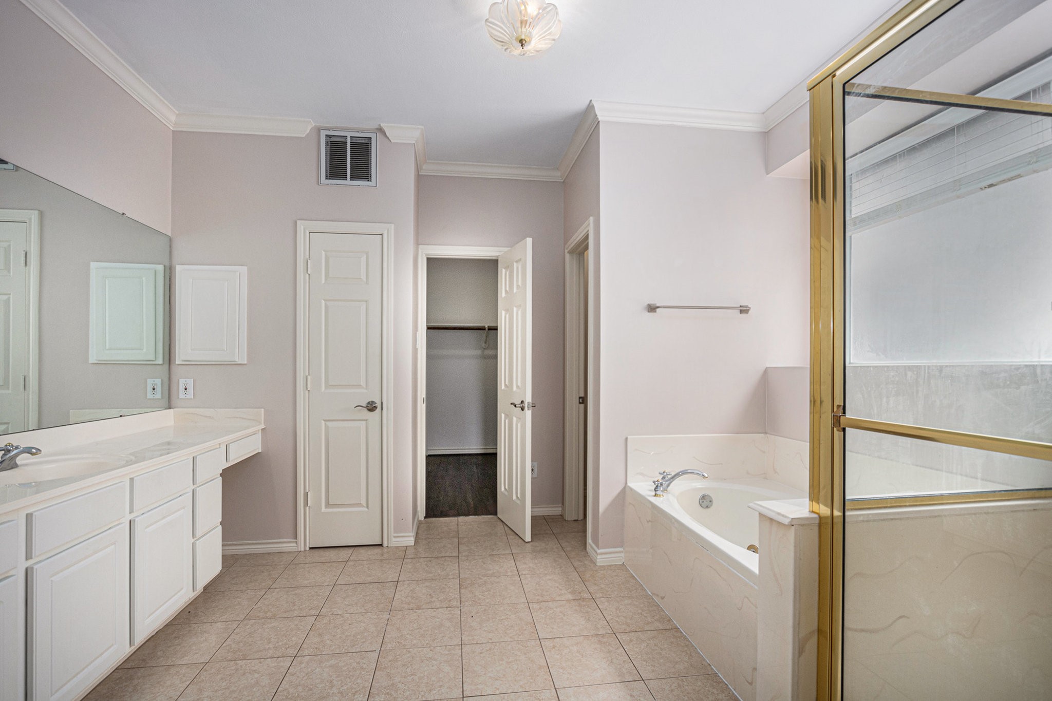 This bathroom features a spacious layout with a large vanity, a soaking tub, and a separate shower. It has neutral tile flooring and ample natural light, creating a bright and inviting space.