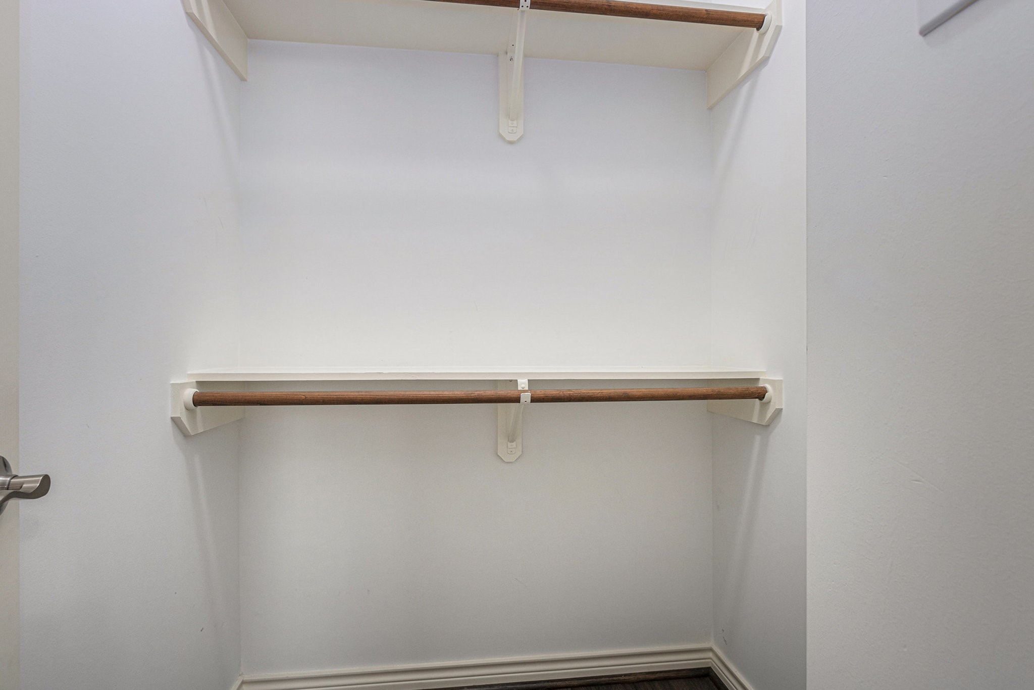 This photo shows a walk-in closet with two wooden hanging rods and white shelves, offering efficient storage space.