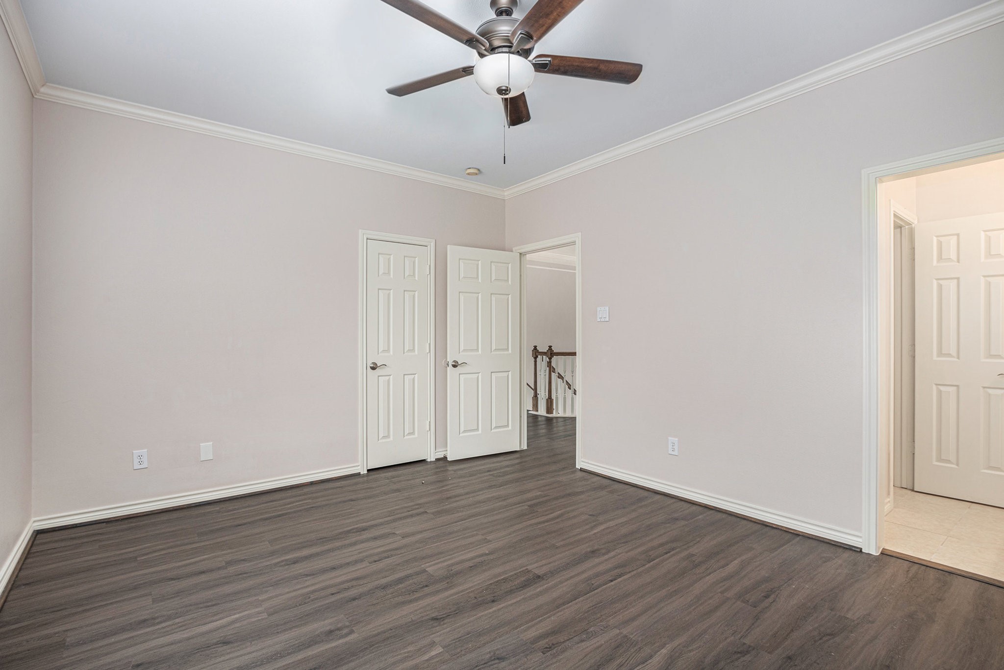This room features sleek dark wood flooring, neutral walls, and a ceiling fan. It includes multiple doors leading to other areas, offering good connectivity within the home.