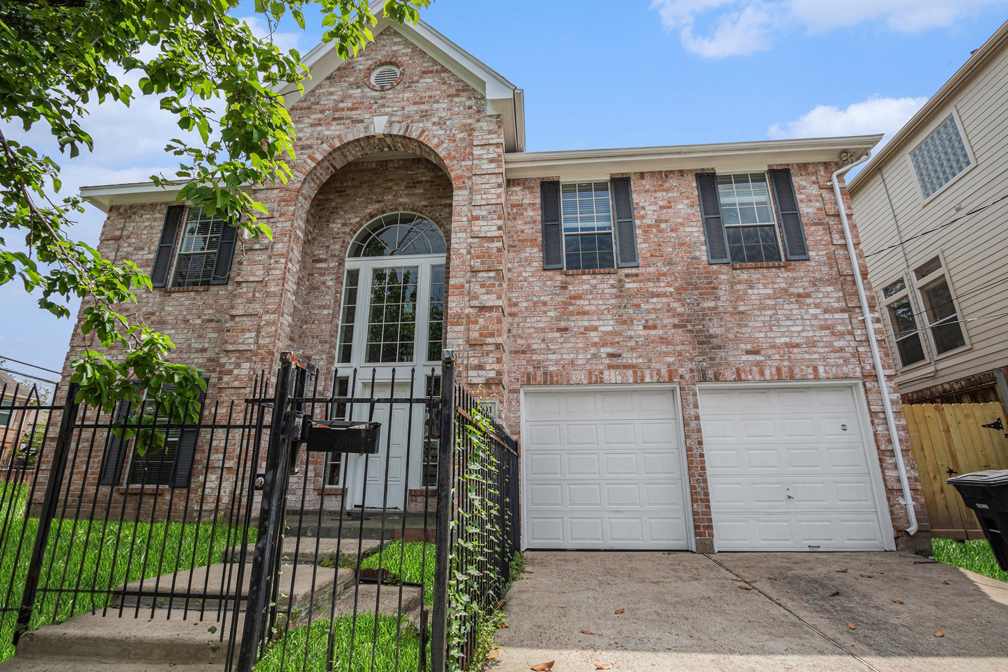 This photo showcases a two-story brick home with an arched entryway and large windows. It features a fenced front yard, a double garage, and a concrete driveway, offering a welcoming and secure exterior.