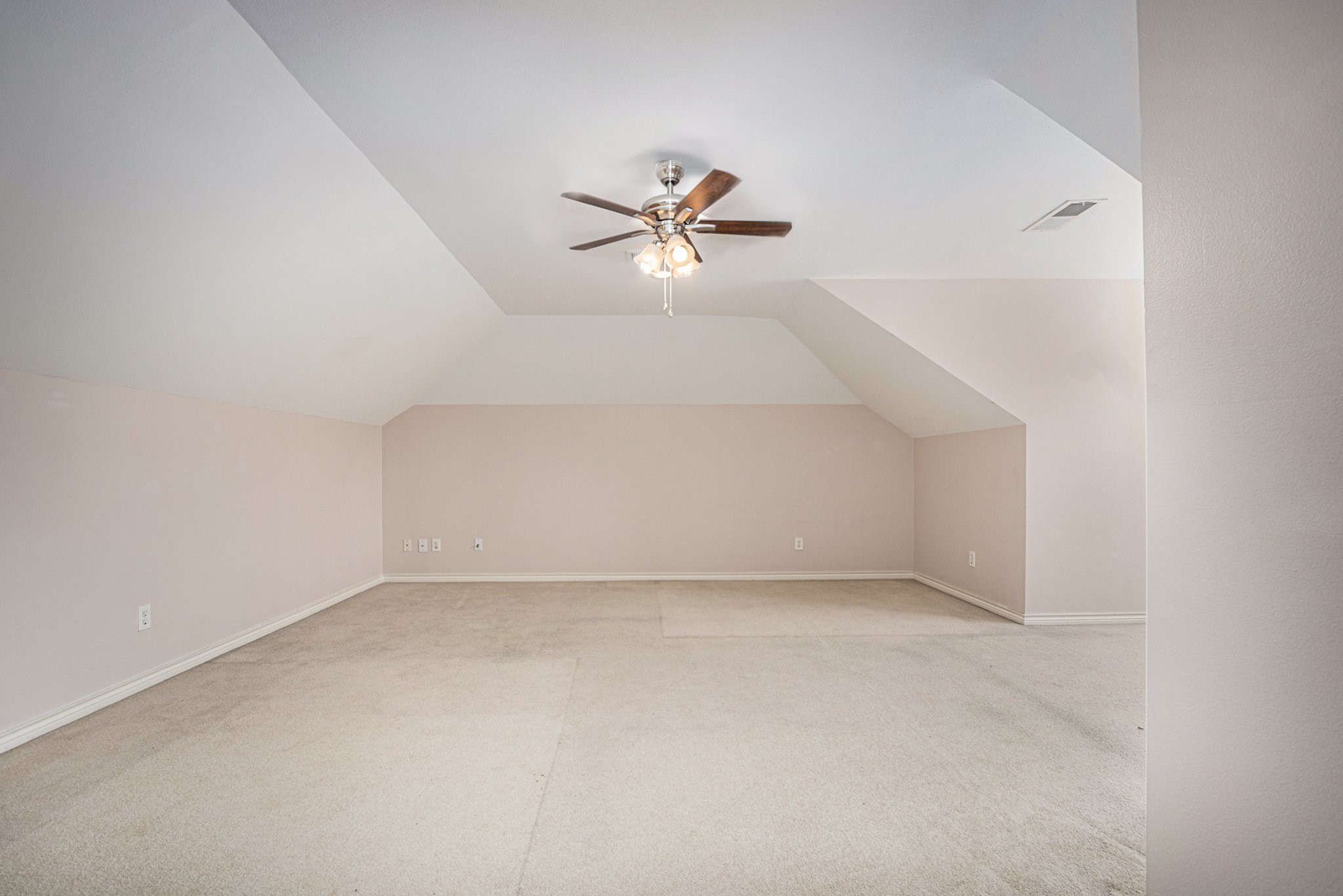 This spacious room features light-colored walls, a sloped ceiling, and a ceiling fan with lights, offering a versatile area for customization.