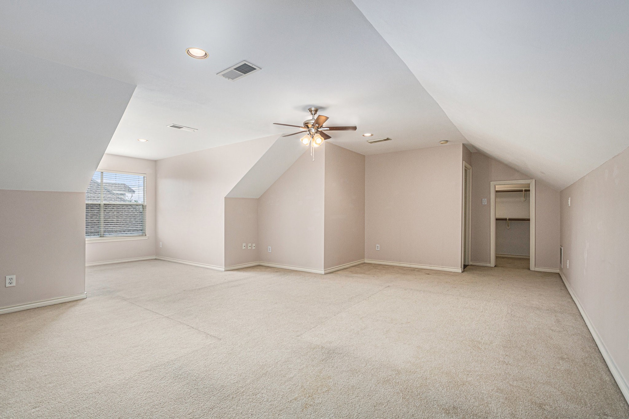 This spacious room features neutral carpeting, sloped ceilings, recessed lighting, and a ceiling fan. It includes a window for natural light and a walk-in closet, making it versatile for various uses.