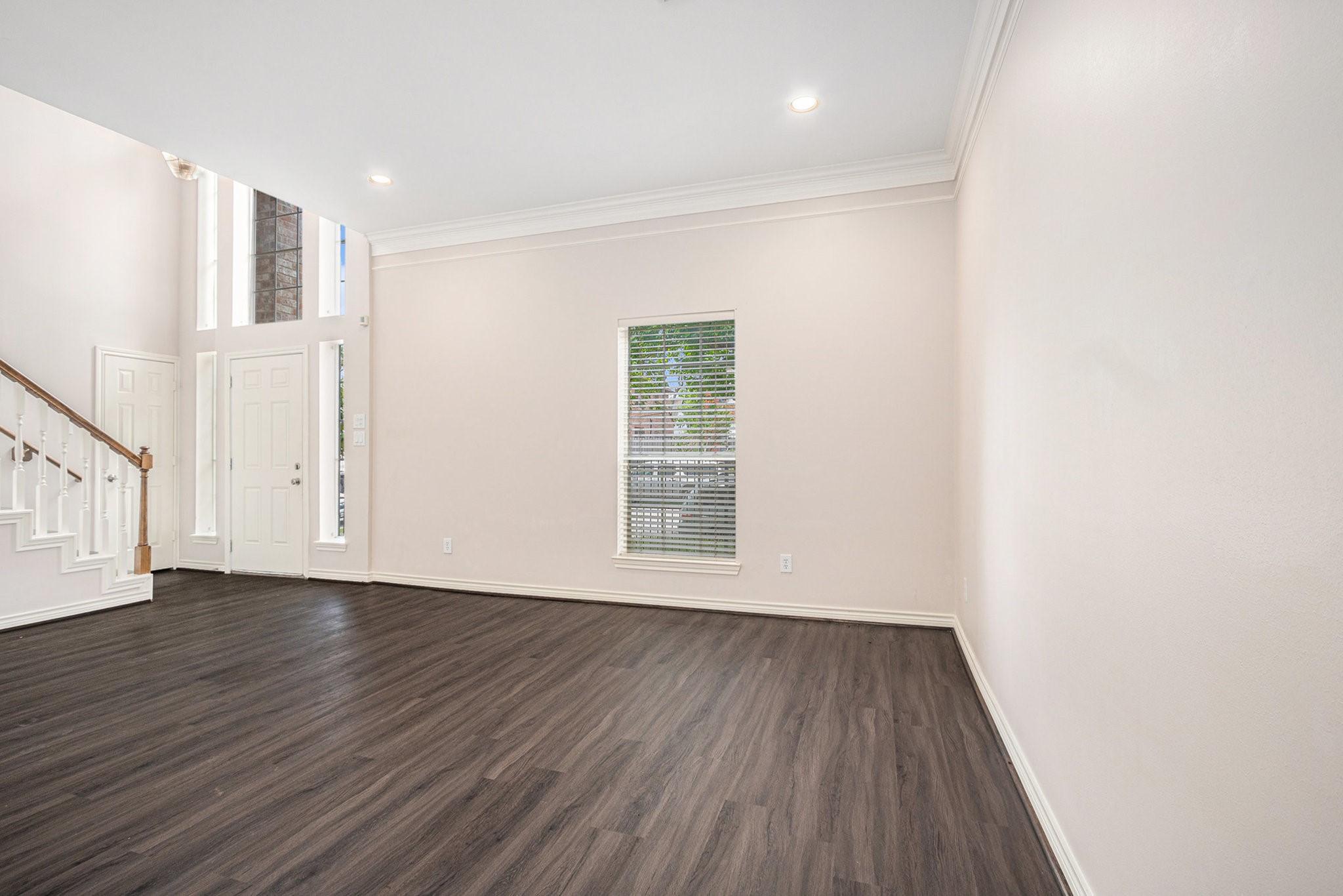 This photo showcases a bright, open living space with high ceilings and large windows. It features dark wood flooring, neutral walls, and an elegant staircase, creating a welcoming and airy atmosphere.