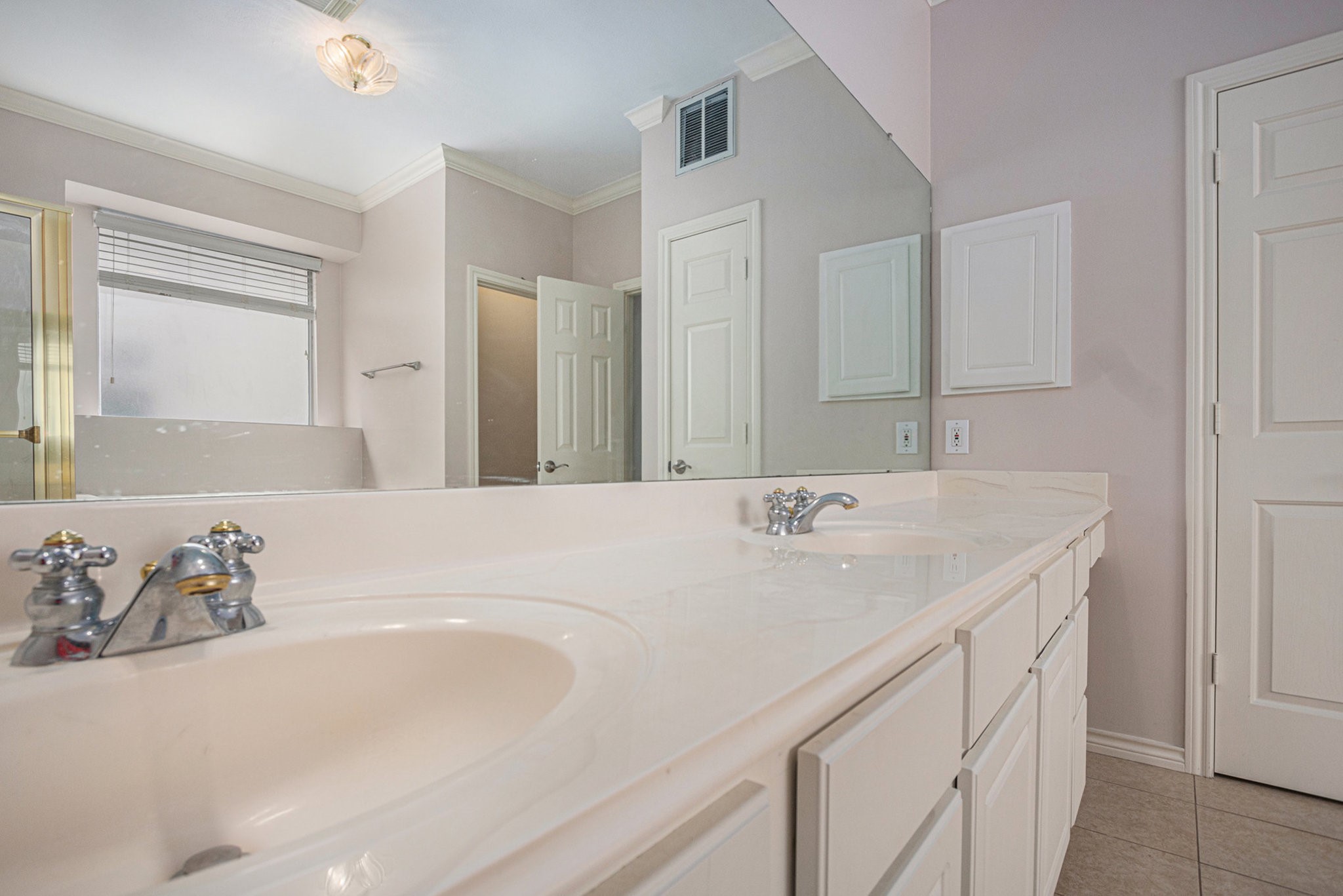 This bathroom features a spacious dual-sink vanity with ample counter space, a large mirror, and neutral tile flooring. The room is well-lit with natural light from a frosted window, offering privacy and elegance.