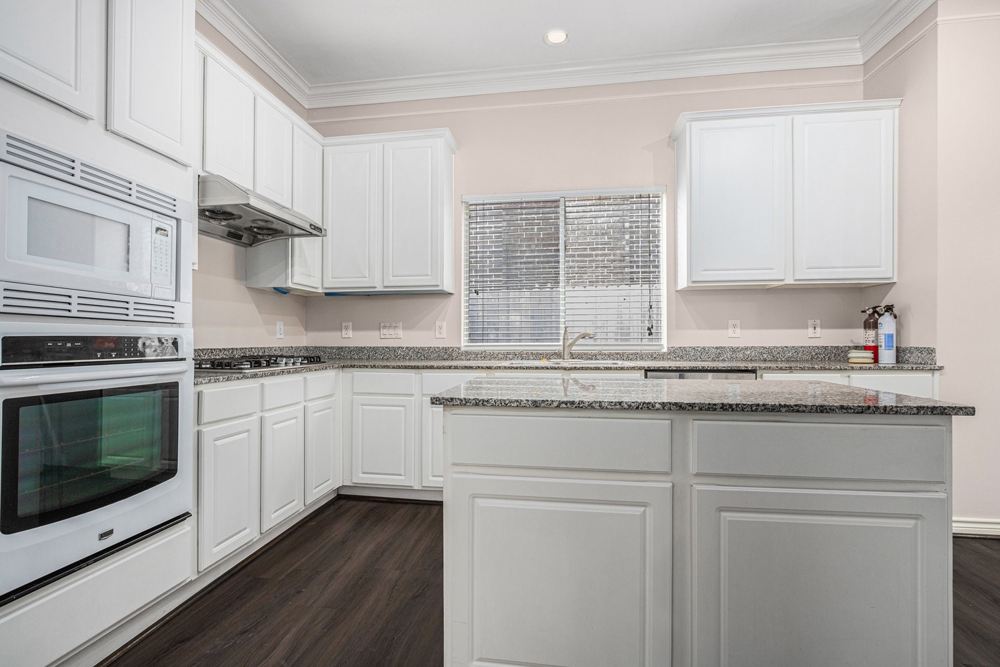 Bright and spacious kitchen with sleek white cabinetry, granite countertops, and modern appliances. The large window provides ample natural light, complementing the elegant dark wood flooring. Ideal for culinary enthusiasts.