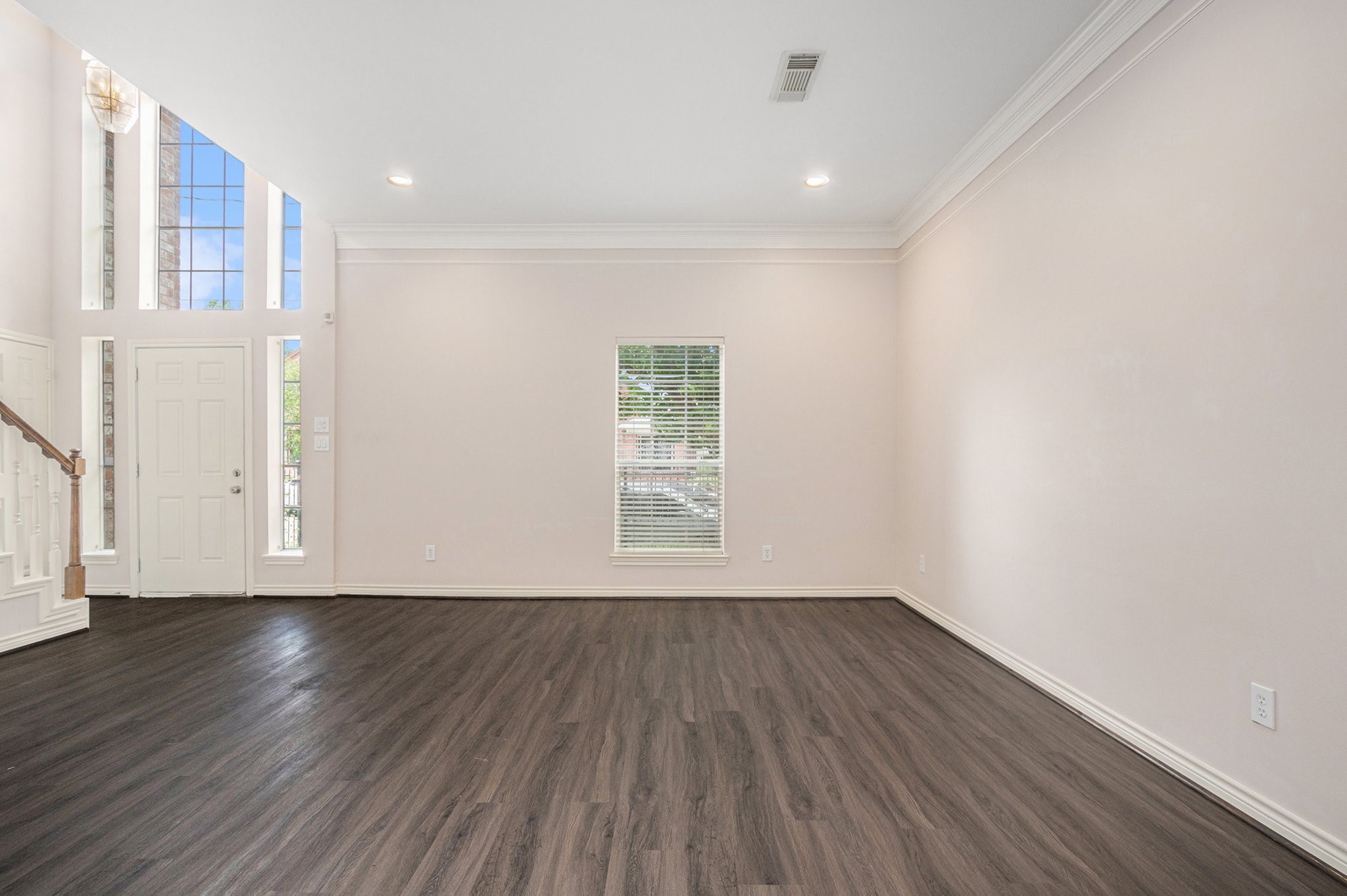 This spacious living area features high ceilings, large windows for natural light, and elegant wood flooring, creating a bright and inviting space.