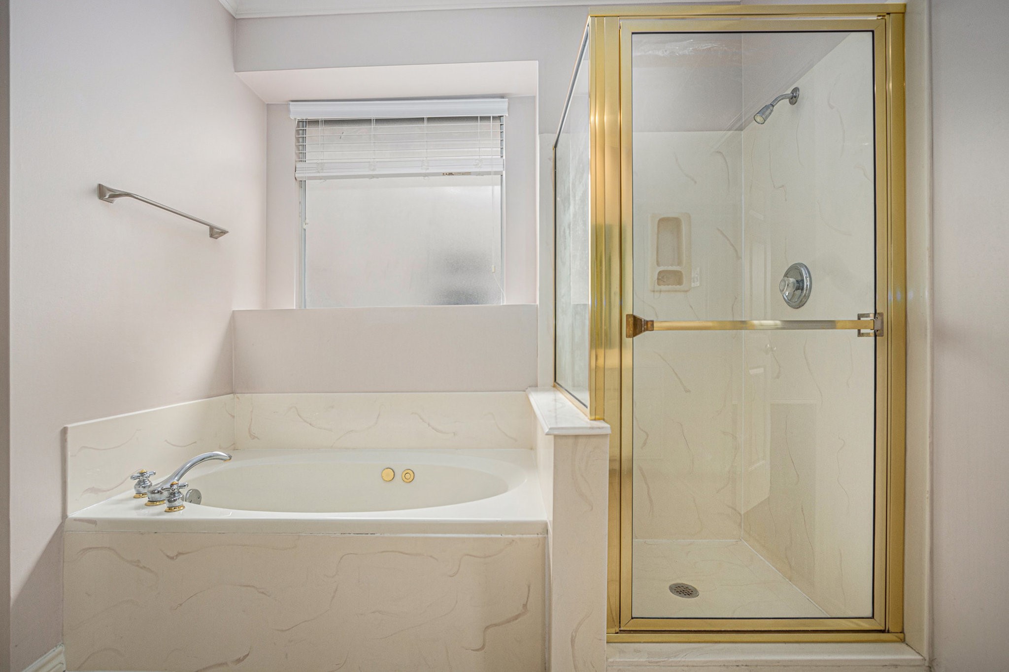 This bathroom features a spacious corner bathtub with sleek fixtures and a separate glass-enclosed shower, accented with gold trim. A frosted window provides natural light while maintaining privacy.
