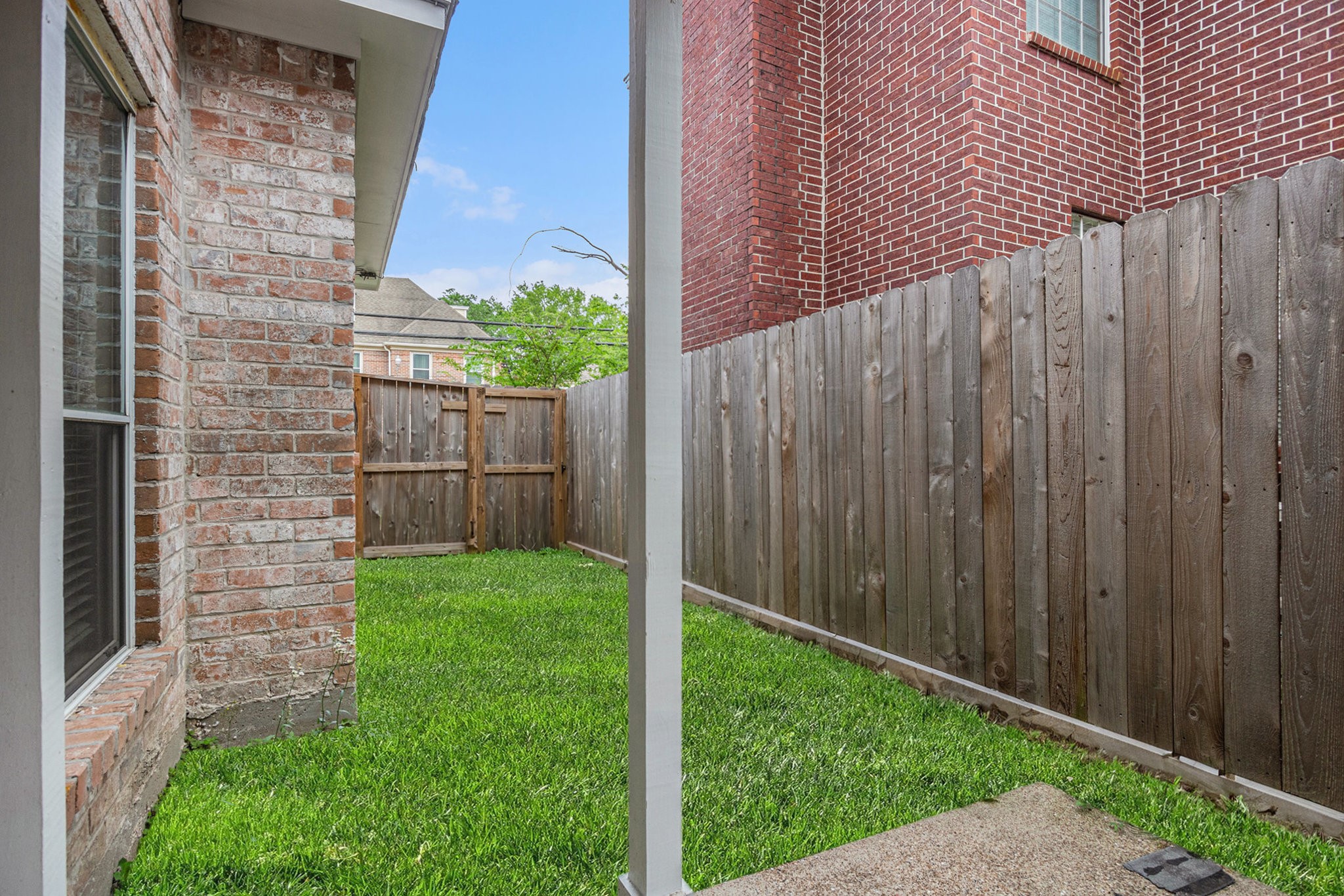 This photo shows a small, fenced backyard with a well-maintained grassy area. It features a brick exterior wall of the house and a wooden fence providing privacy. Ideal for a cozy outdoor space.