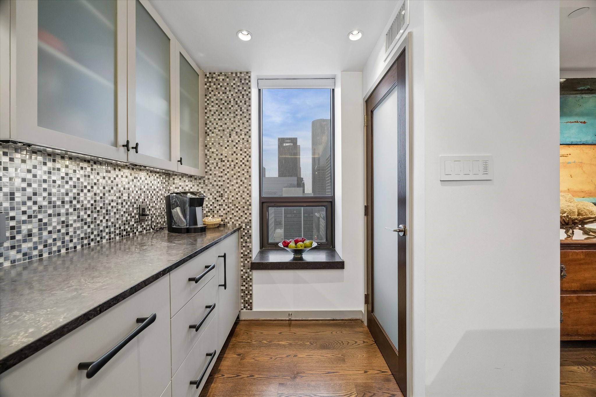 Additional kitchen counter provides a separate surface for preparation or serving. Upper cabinets and lower drawers extend storage, while a narrow window brings in daylight and a city outlook.