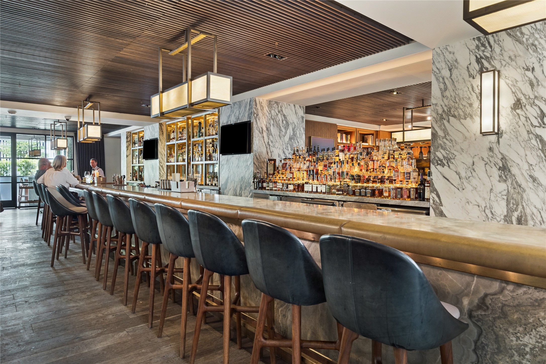 Hotel bar provides a setting for drinks and conversation beyond the coffee counter. Stone surfaces, wood finishes and integrated lighting distinguish the bar area.
