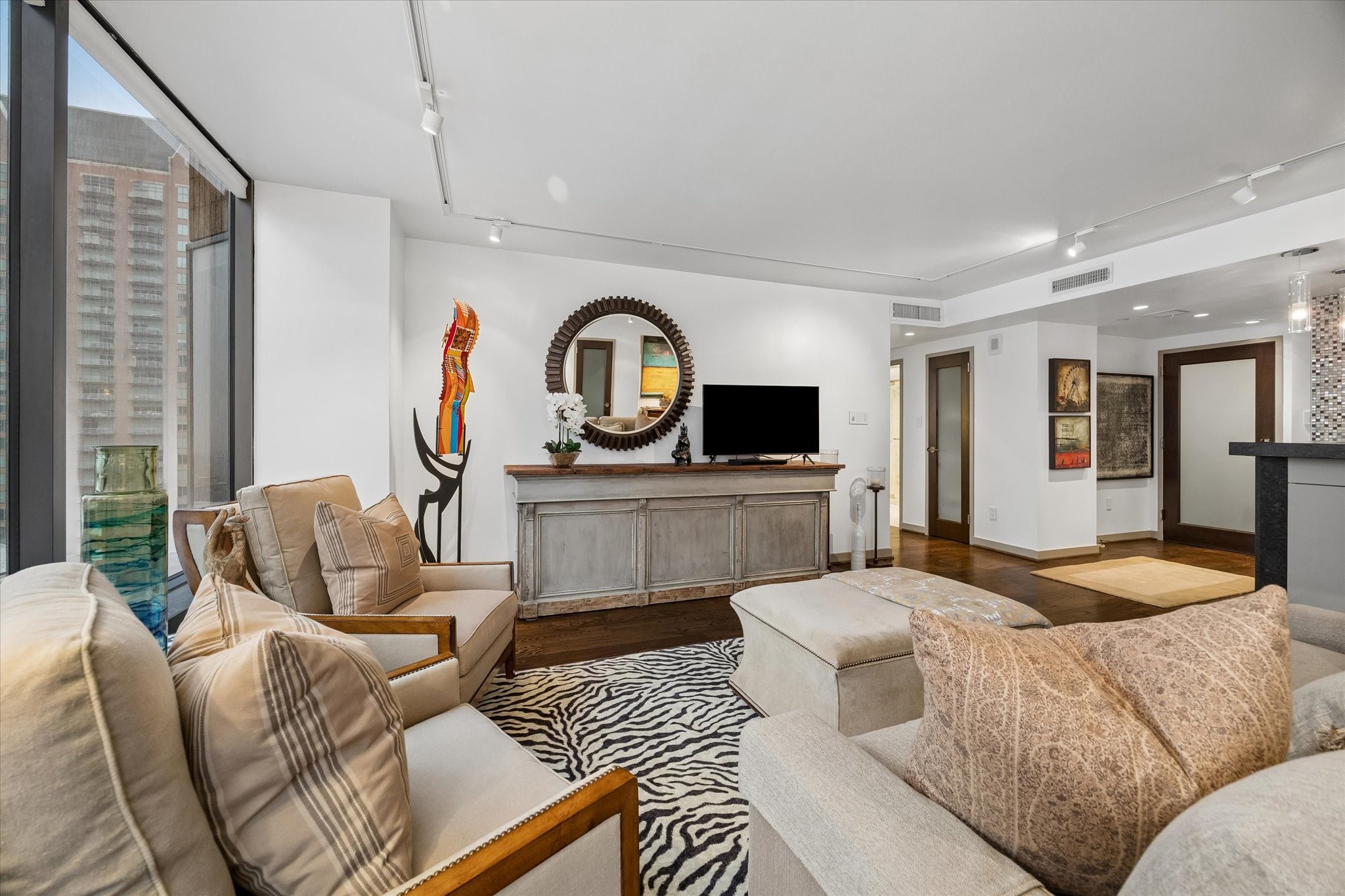 Reverse living room view shows the connection to the entry and kitchen. Continuous wood flooring and track lighting tie the main living spaces together.