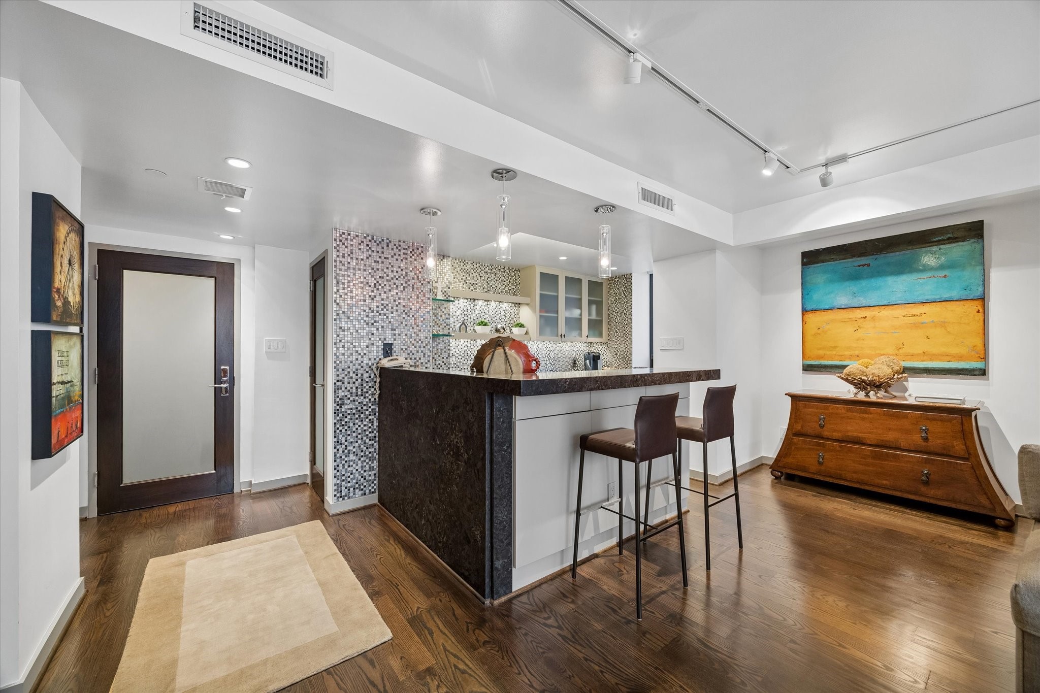 Breakfast bar creates a transition between meal preparation and the living area. Stone counters, mosaic backsplash and glass front cabinetry carry the kitchen finishes across the open plan.