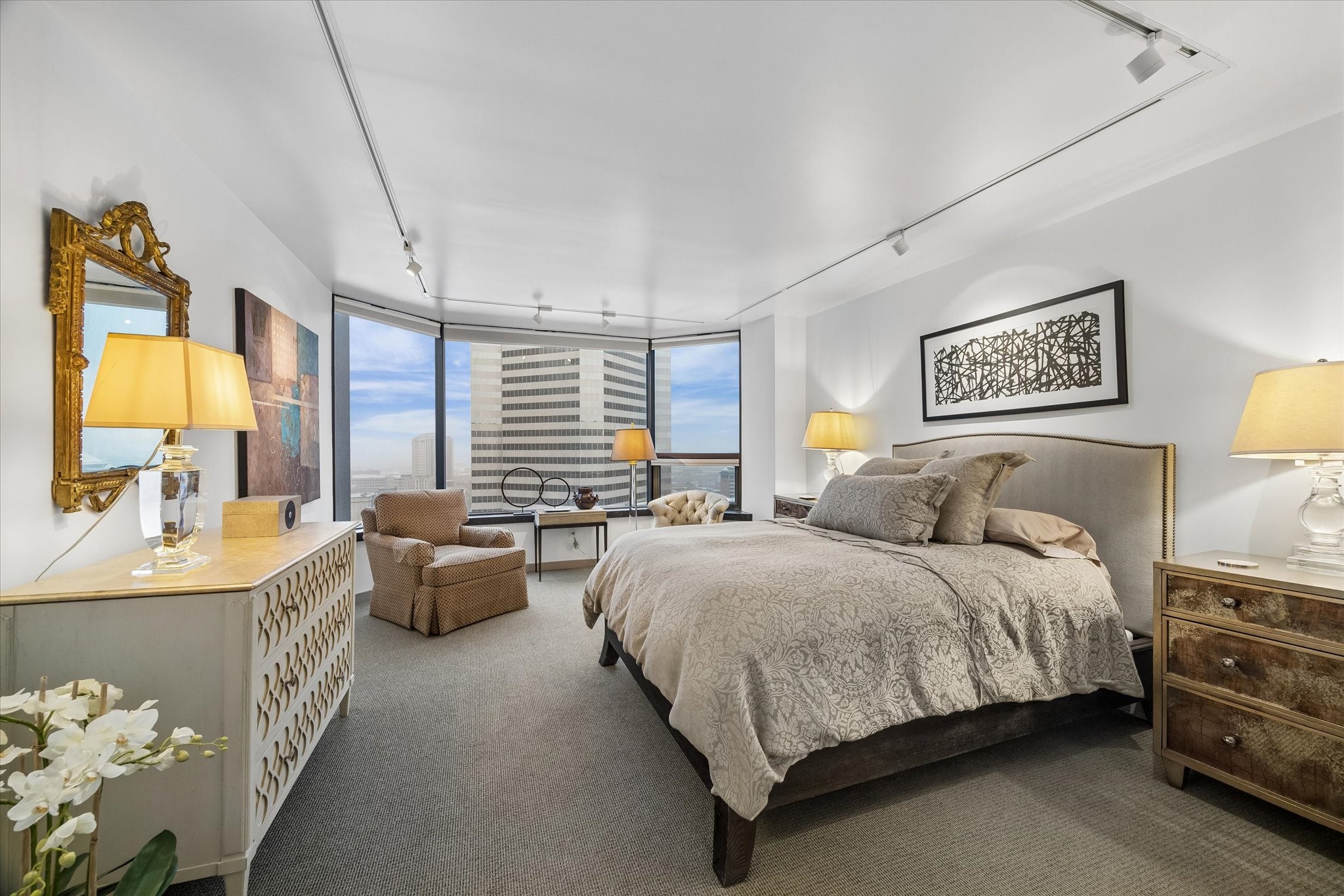 Bedroom windows frame the downtown skyline, with automated Lutron shades for light control and privacy. Carpet distinguishes the sleeping area from the wood floors in the main living space.