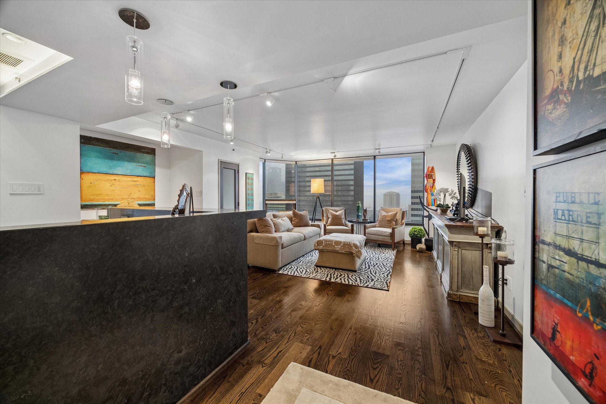 Open sightlines link the kitchen and living area, allowing conversation to continue across both spaces. Pendant lighting marks the breakfast bar while city views draw the eye toward the windows.
