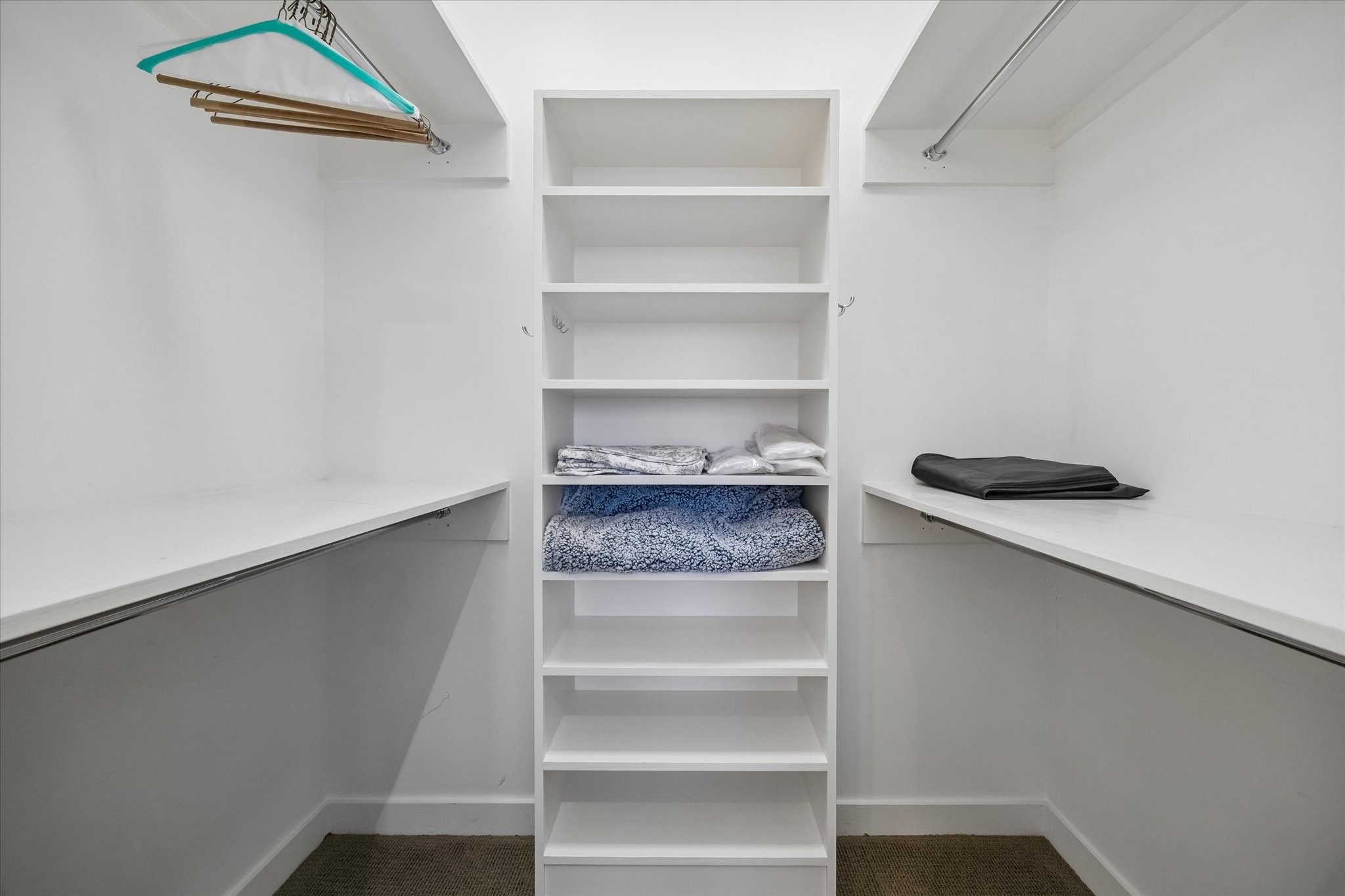Shelving and hanging rails line both sides of the walk in closet, separating folded items from hanging storage and keeping the center aisle clear.
