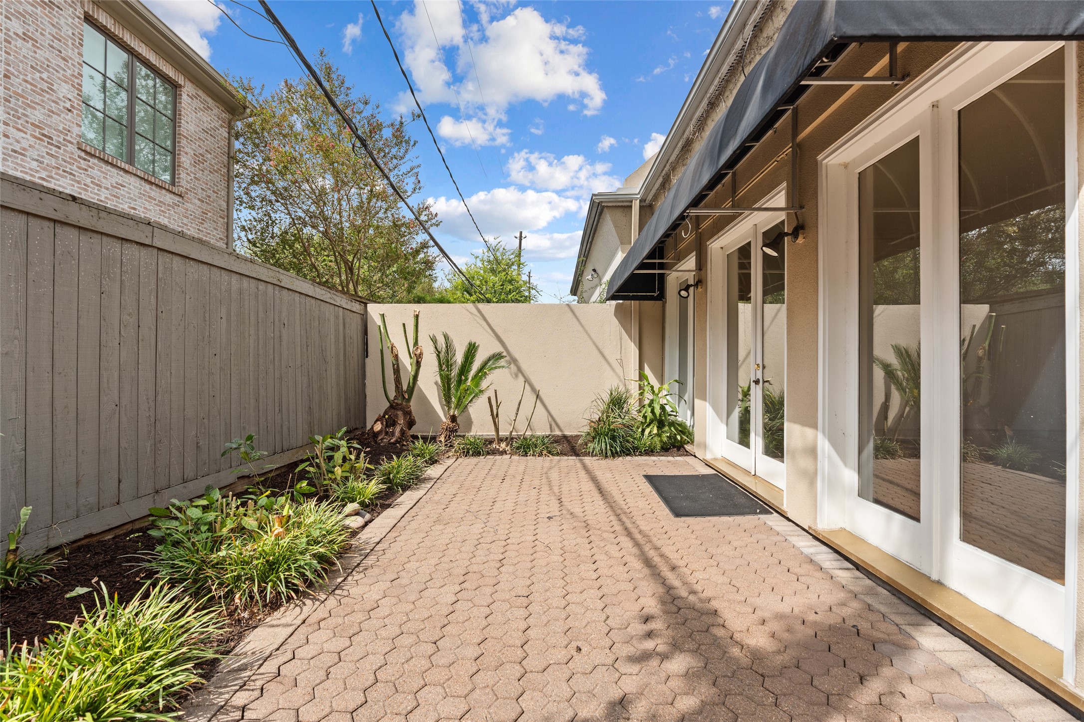 Charming back private patio with brick pavers, lush landscaping, and elegant French doors, perfect for outdoor relaxation and entertainment.