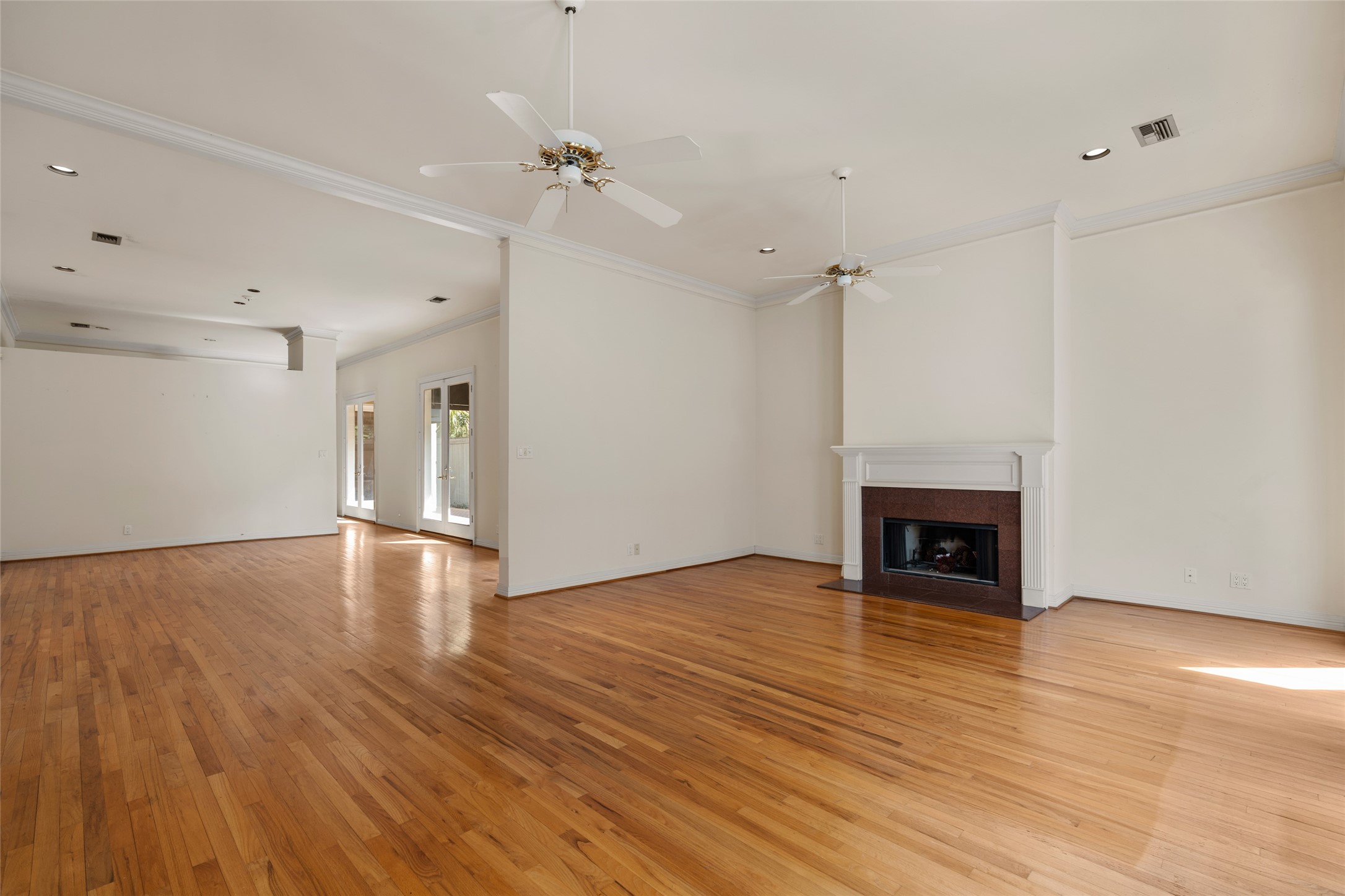 Spacious and bright living area with polished hardwood floors, a cozy fireplace, leading to a sunlit outdoor space through glass doors.