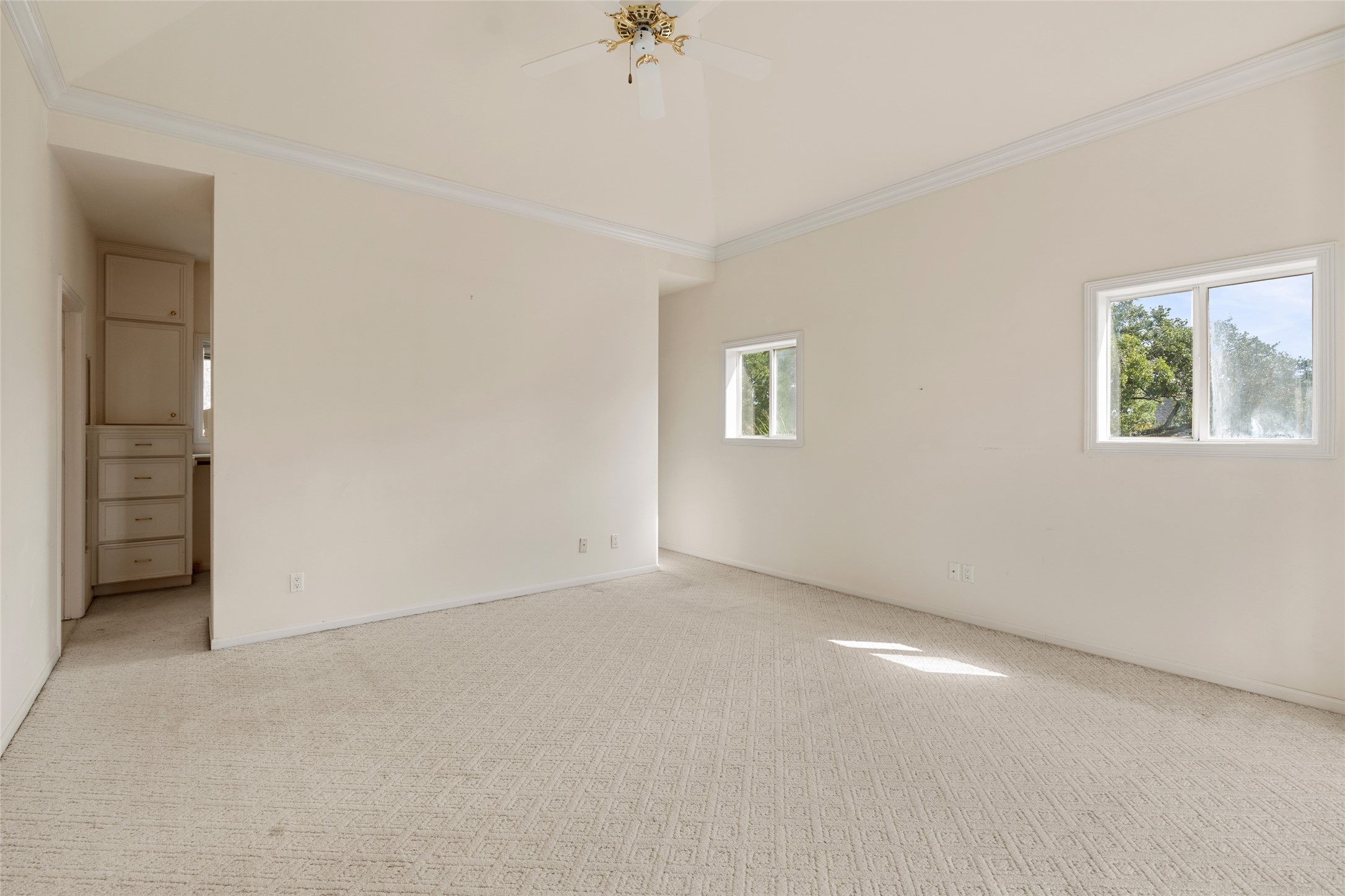 Very spacious primary room with neutral tones, featuring a vaulted ceiling and natural light from two windows, offering a serene and airy atmosphere.