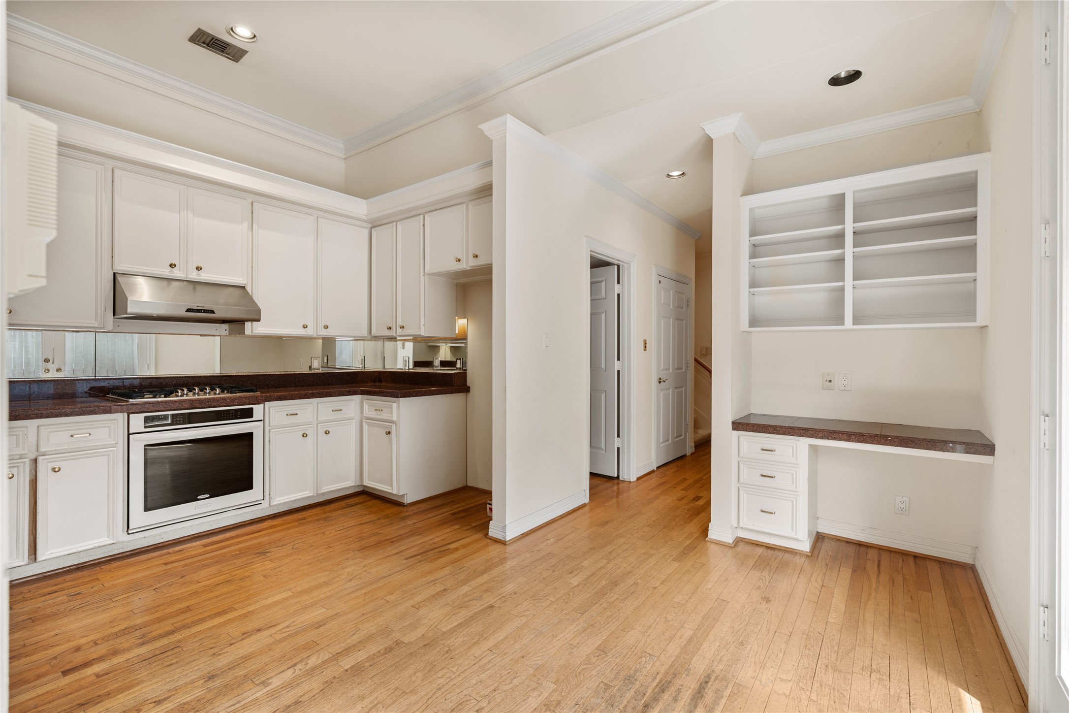 Bright and spacious kitchen with hardwood floors, ample cabinetry, and a built-in cooktop. A cozy nook with built-in shelving and desk provides extra storage and workspace. NOTE: Powderbath, elevator, stairs, laundry and garage located and office area located just past kitchen area.