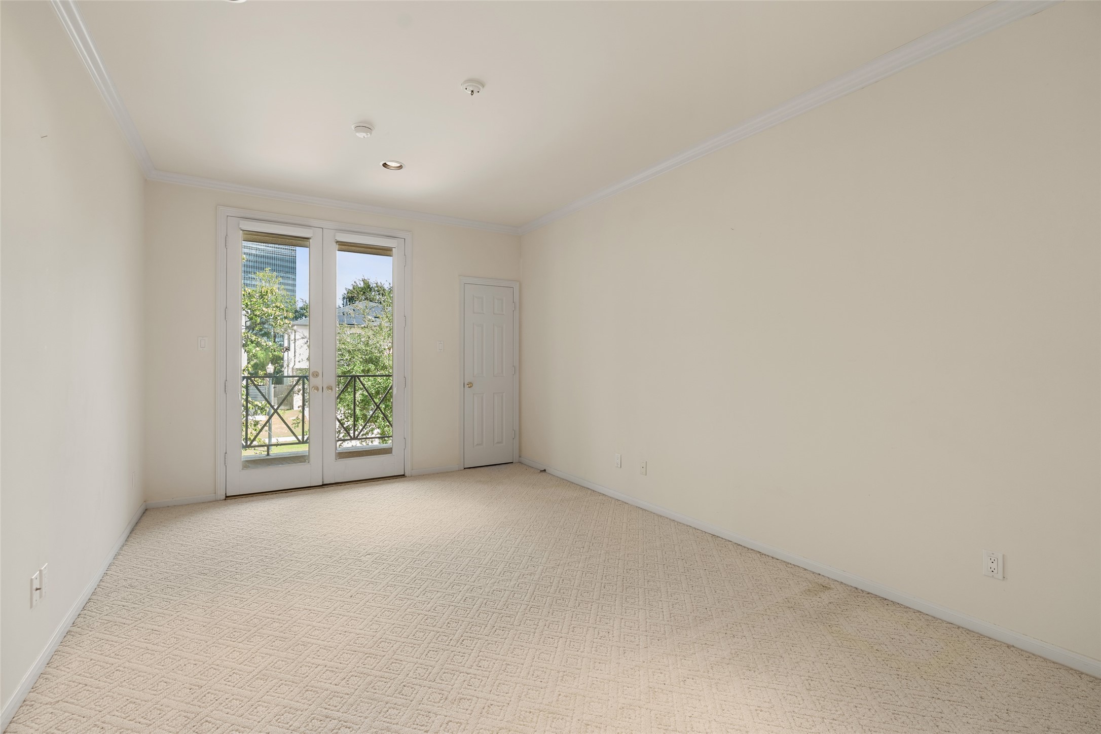 Bright and spacious room featuring elegant French doors that open to a charming balcony, offering a serene view of lush greenery.