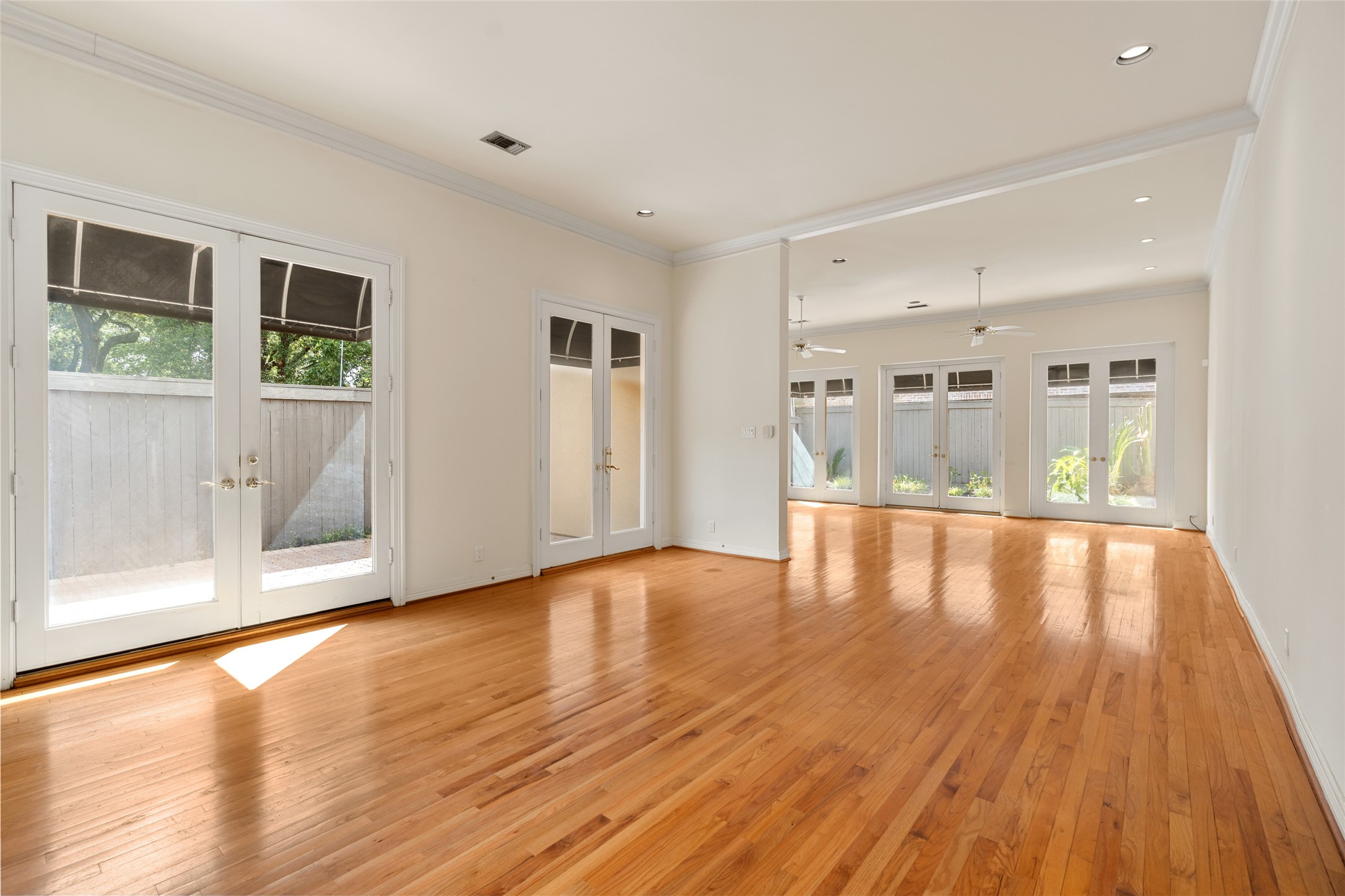 Spacious and bright open living area with gleaming hardwood floors, abundant natural light from multiple French doors, and elegant ceiling fans.