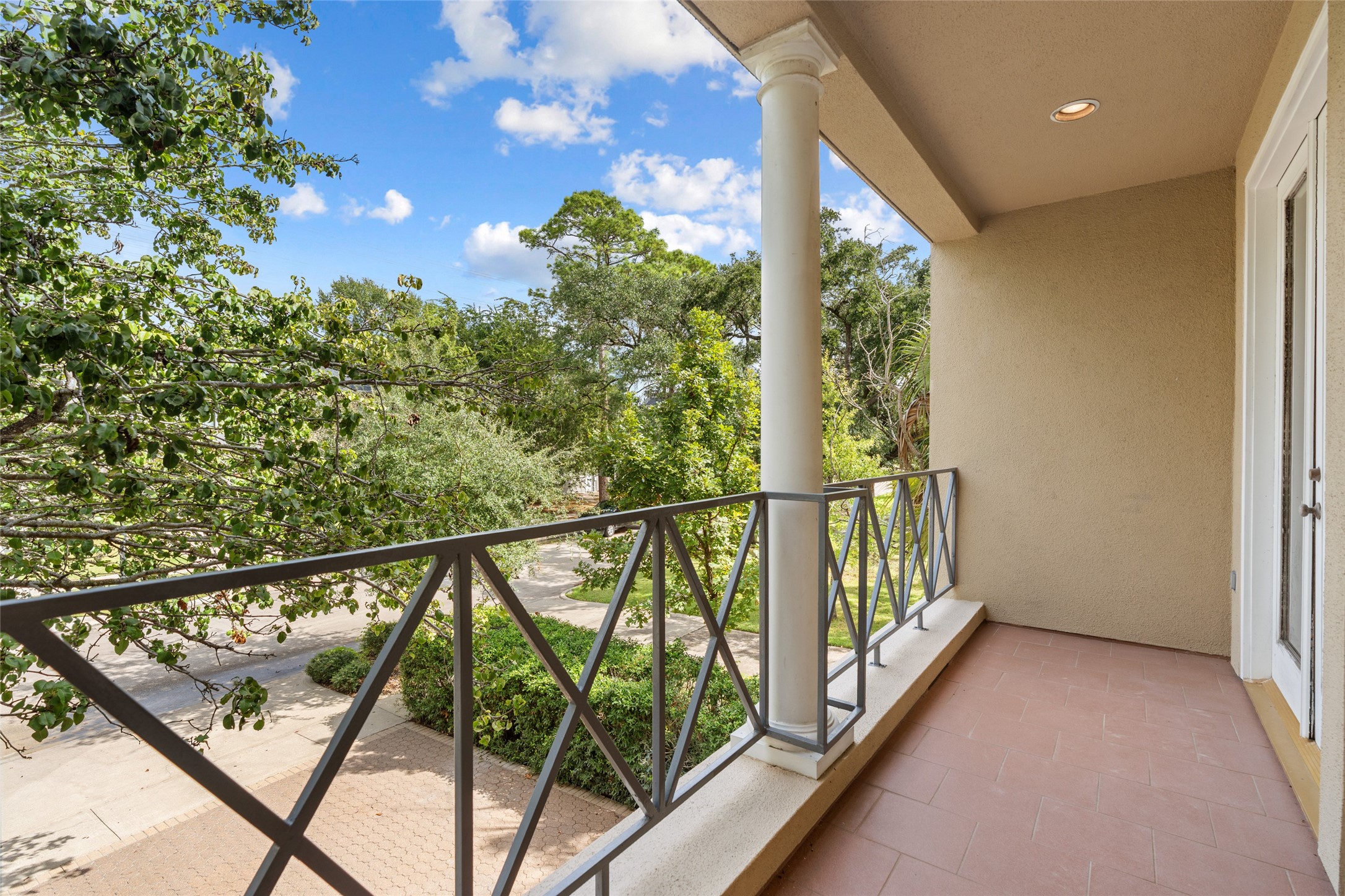 Charming front balcony off bedroom with elegant railings and a serene view of lush greenery, perfect for relaxing outdoors.