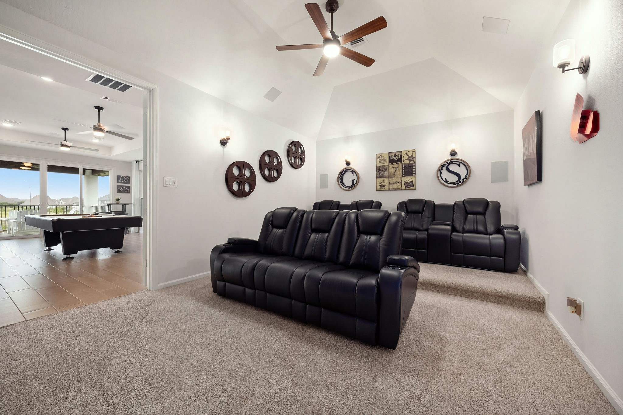 A dedicated home theater delivers a cinematic experience with full surround sound speakers, a subwoofer, ambient uplighting, and a ceiling fan, complemented by elevated tiered flooring designed for an immersive movie-watching experience