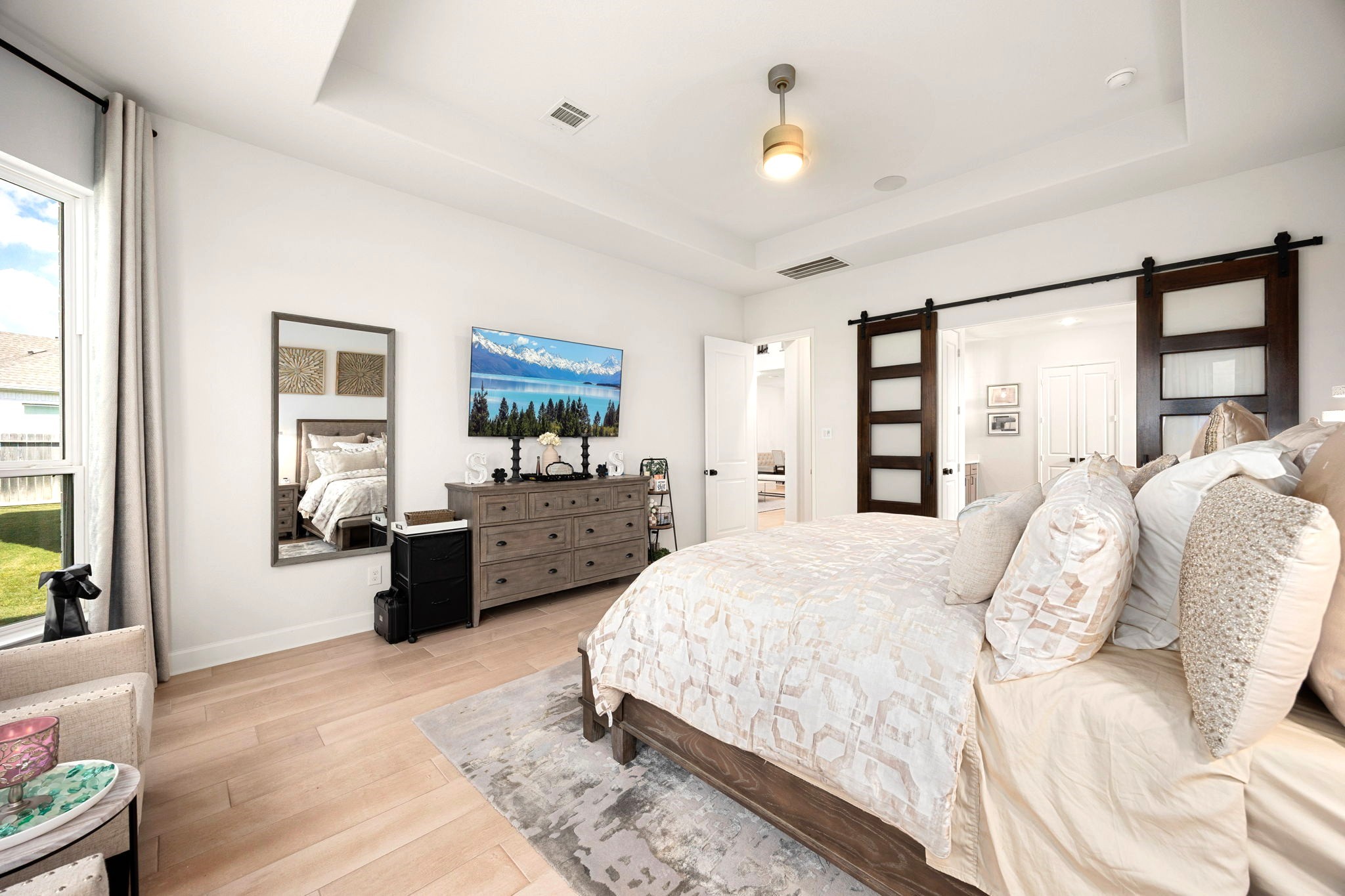 Elegant double sliding barn doors create a striking transition from the spacious primary bedroom to the luxurious ensuite bathroom, adding custom architectural character and a sophisticated modern touch to the private retreat.