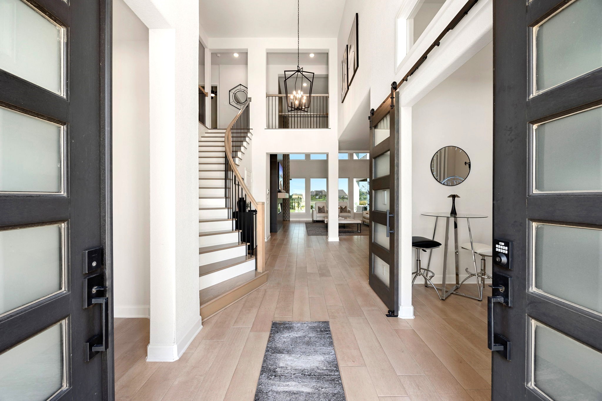 Make a grand first impression with soaring ceilings, a dramatic staircase, and an elegant entryway that sets the tone for this exceptional J. Patrick luxury home. To the right, a custom sliding barn door reveals a private office space, blending architectural elegance with thoughtful functionality.