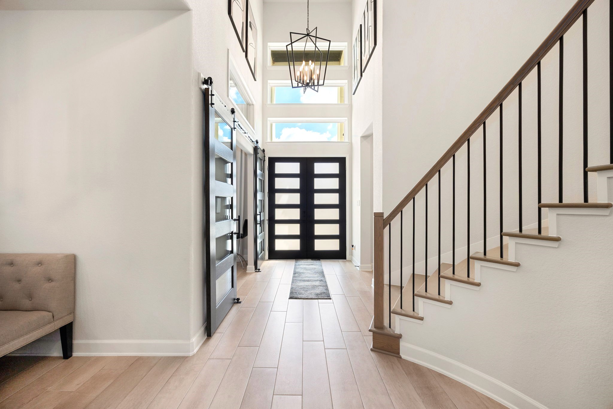 An impressive interior perspective showcases the upgraded double entry doors featuring a smart home locking system, complemented by an elegant upgraded iron staircase that adds architectural sophistication. To the right, a private secondary bedroom with its own ensuite bath offers comfort and privacy for guests or multigenerational living.