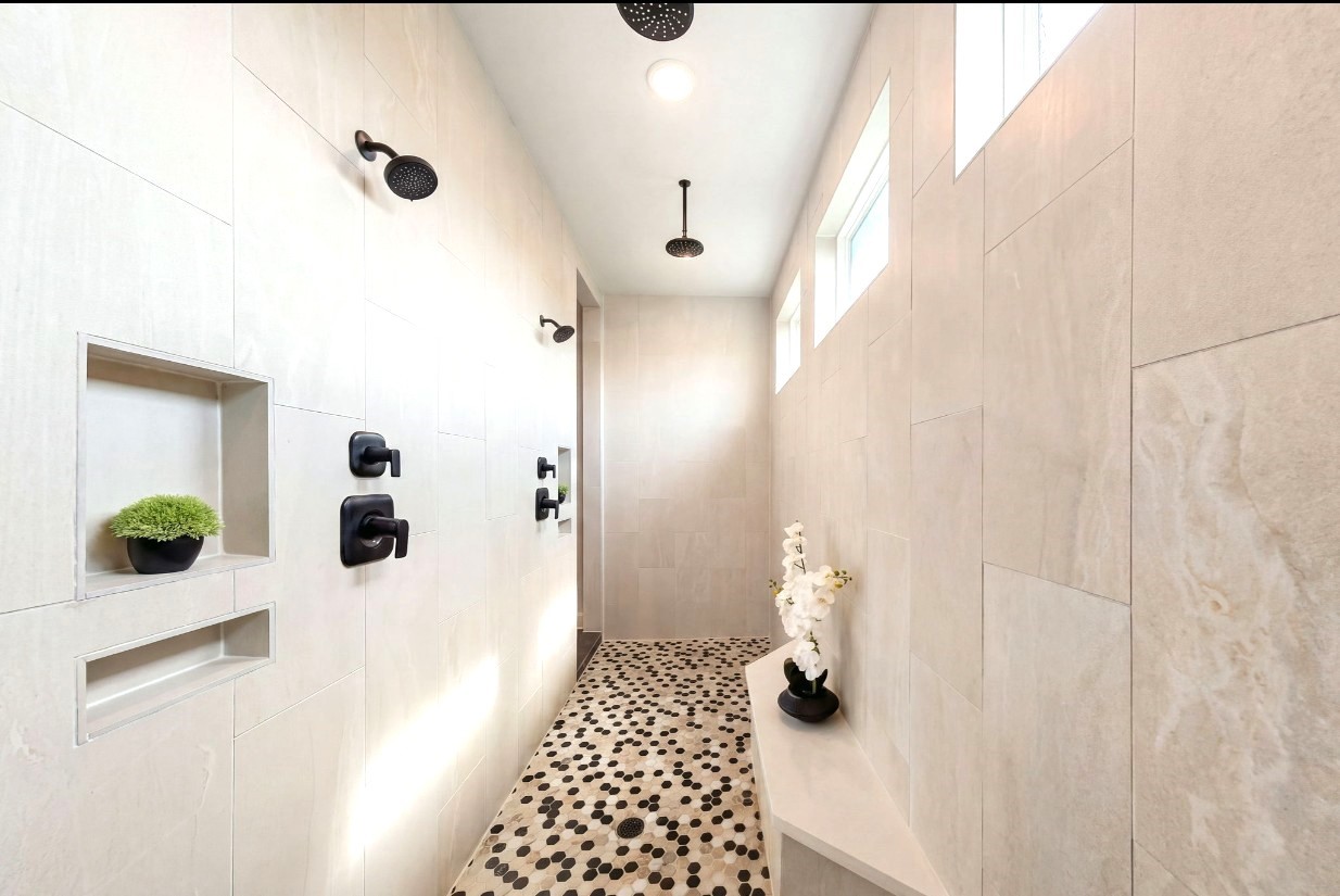 An expansive spa-inspired shower features elegant honeycomb tile, a built-in shower niches and bench, and four upgraded showerheads, including dual overhead rain showers and two wall-mounted showerheads with dual controls for a luxurious, customized bathing experience.