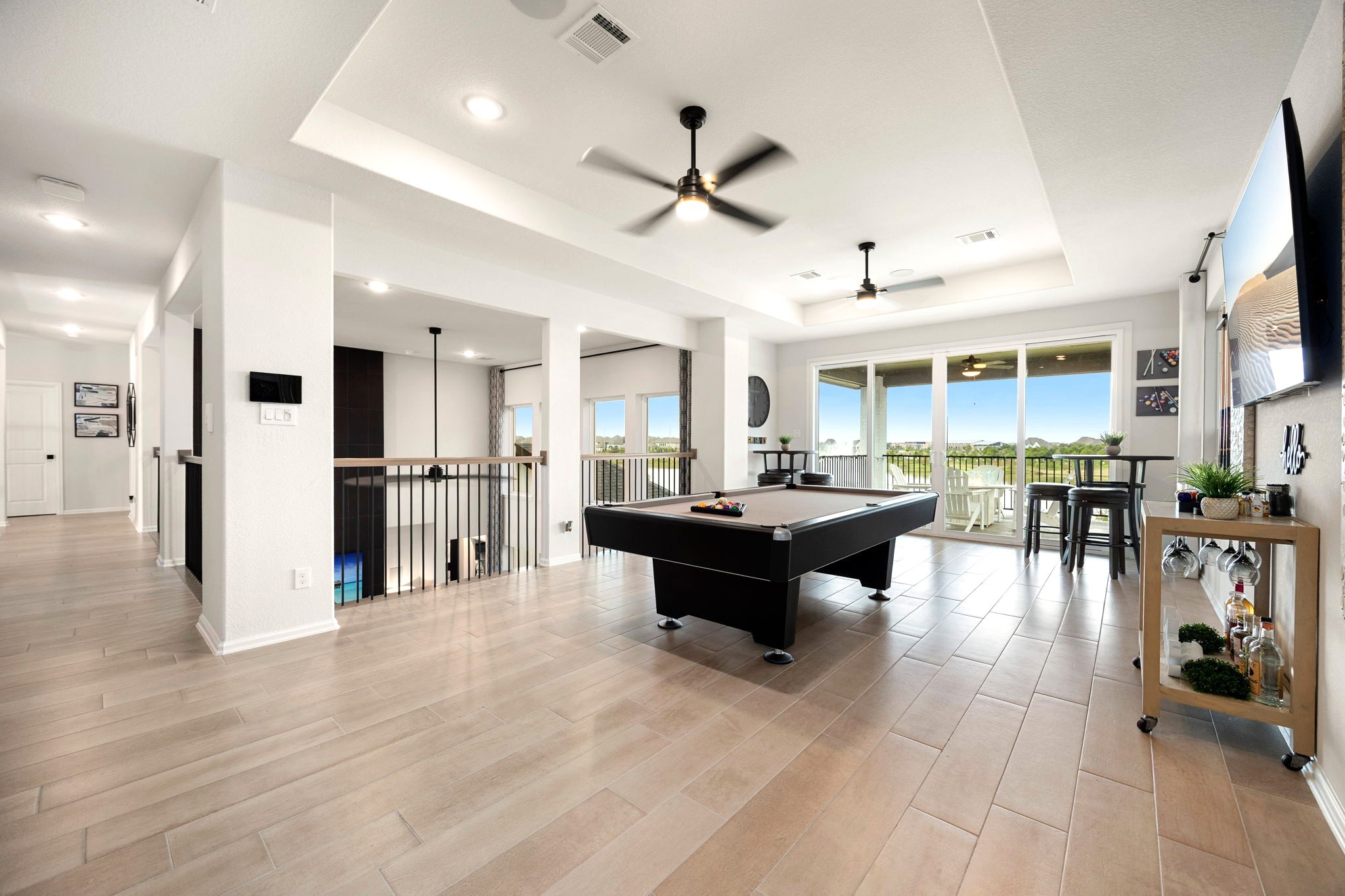 An expansive upstairs game room features a pool table as its centerpiece, with sliding glass doors opening to a second-floor covered balcony overlooking the lake, creating the perfect setting for elevated entertaining, relaxation, and indoor-outdoor enjoyment.