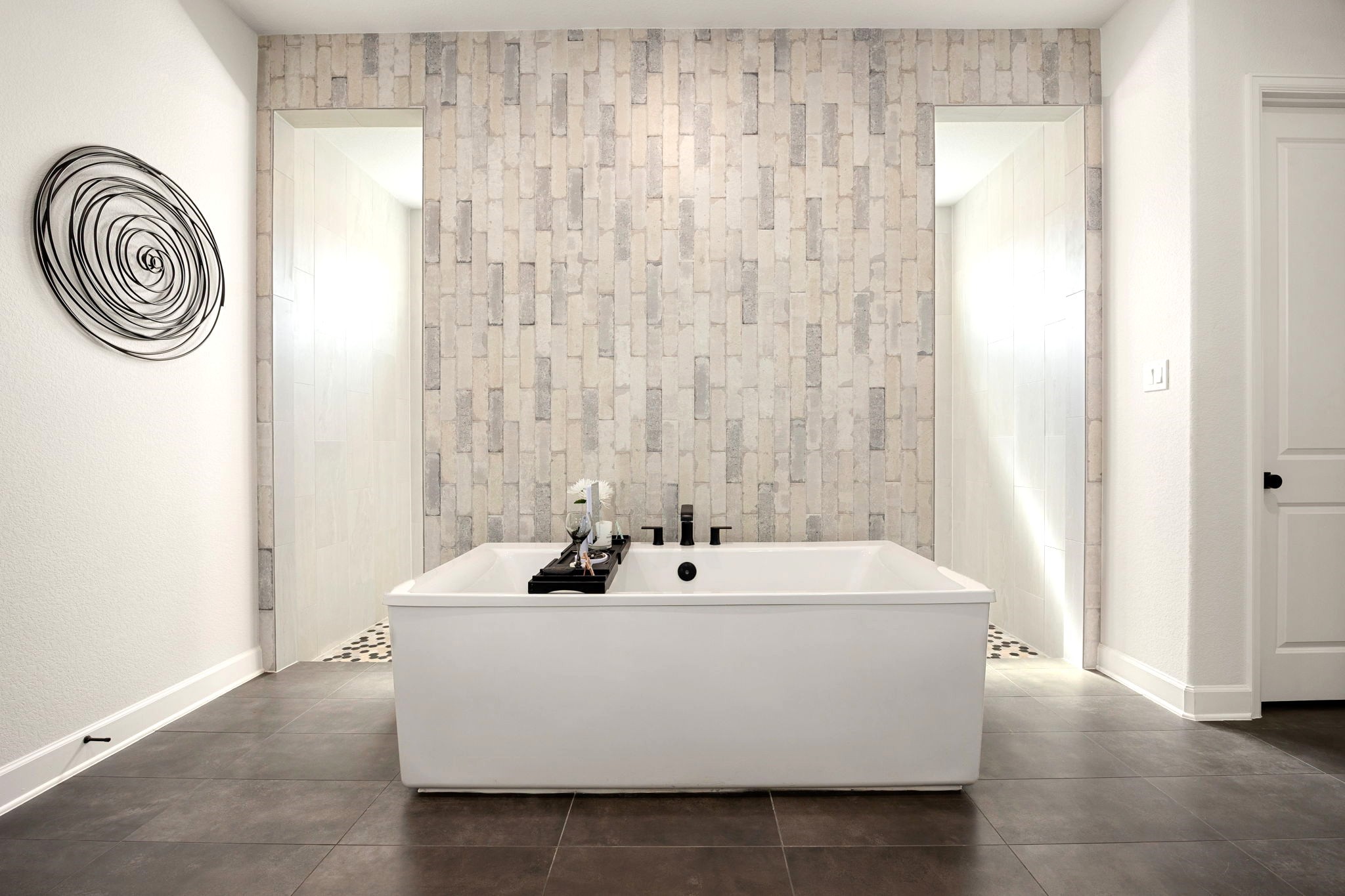 A spa-inspired primary bath showcases an impressive double-entry shower with floor-to-ceiling custom tilework, beautifully complemented by a freestanding soaking tub positioned in front of the striking tiled feature wall for the ultimate luxury retreat.