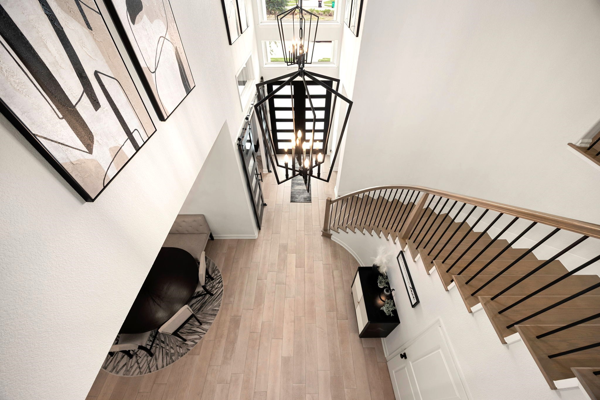 A breathtaking second-floor perspective showcases the grand iron staircase and elegant chandelier suspended above the soaring entryway, highlighting the home's impressive architecture and dramatic two-story design.